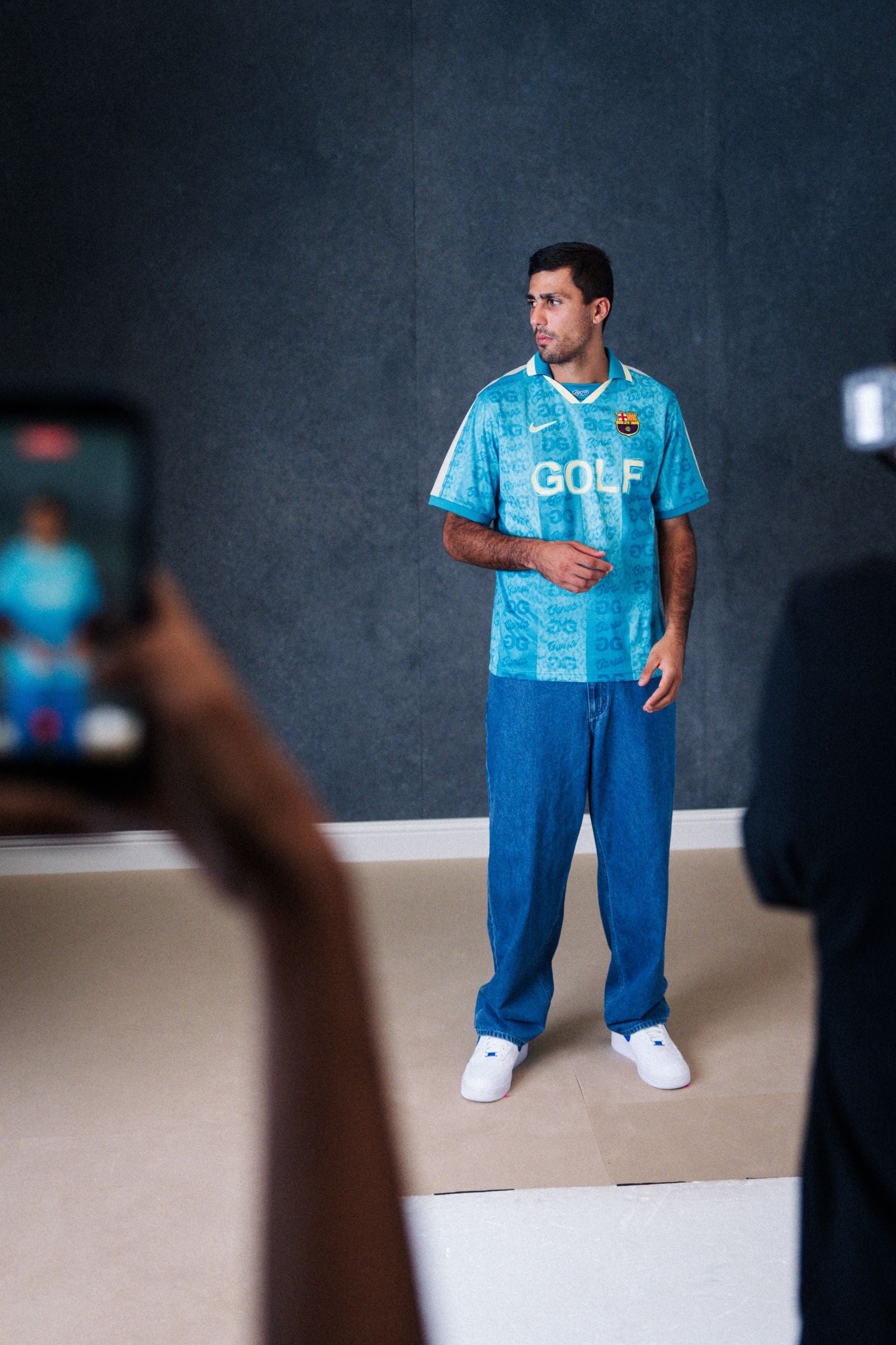 Ein Mann präsentiert das neue blaue Sondertrikot vom FC Barcelona vor dunklem Hintergrund.