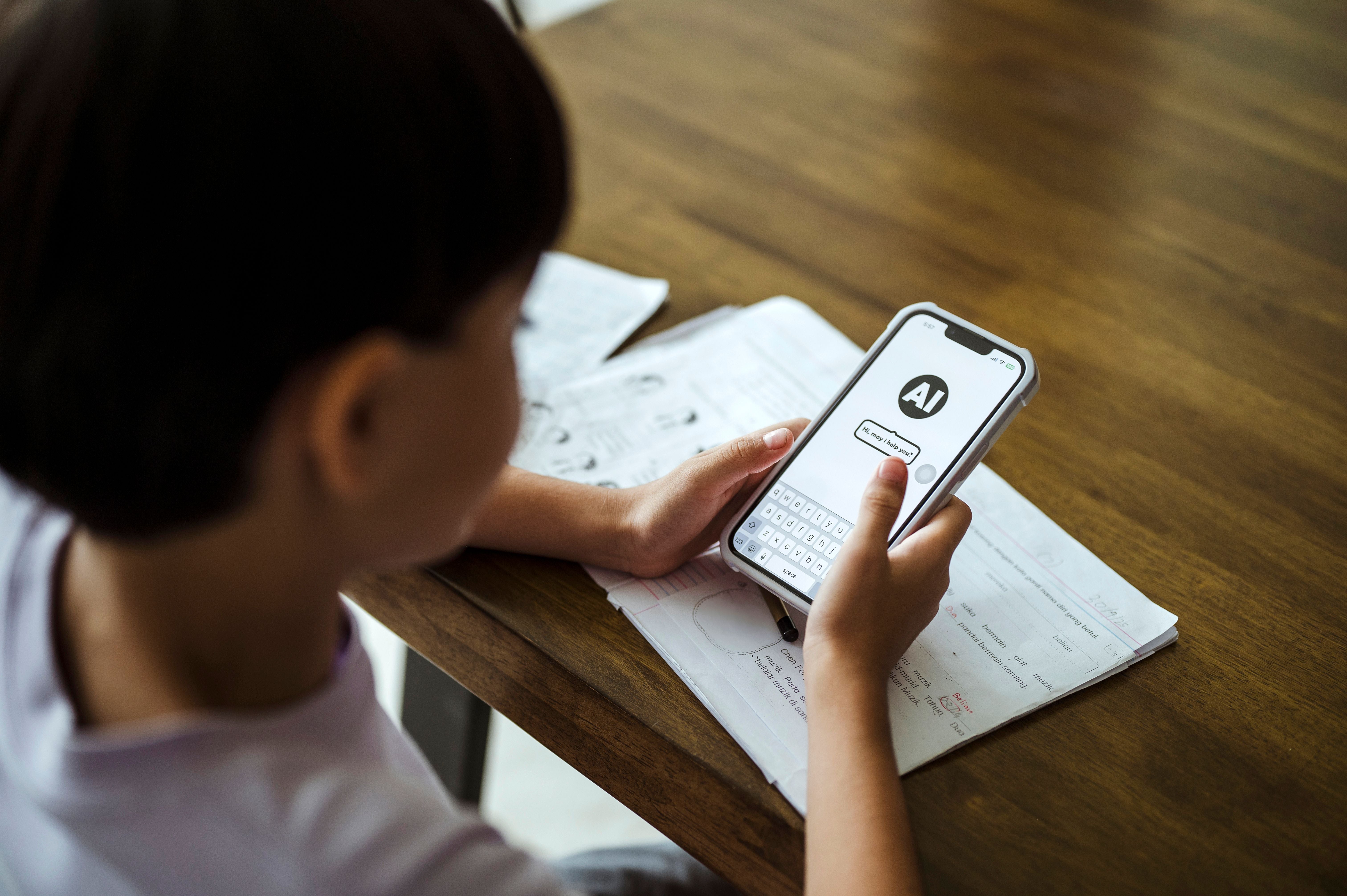 Ein Kind nutzt ein Smartphone mit KI-Unterstützung beim Lernen an einem Schreibtisch mit Schulheften.