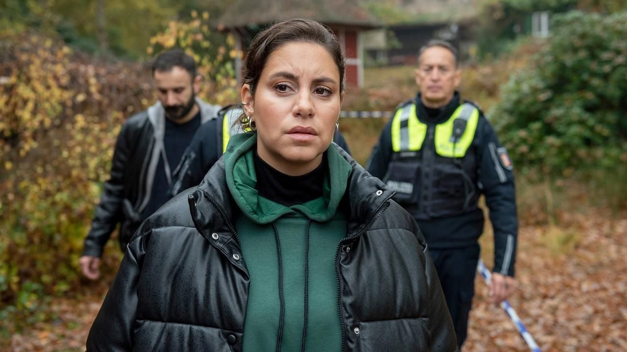 Eine Frau im Vordergrund, dahinter zwei Männer, einer davon in Polizeiuniform, im herbstlichen Freien.
