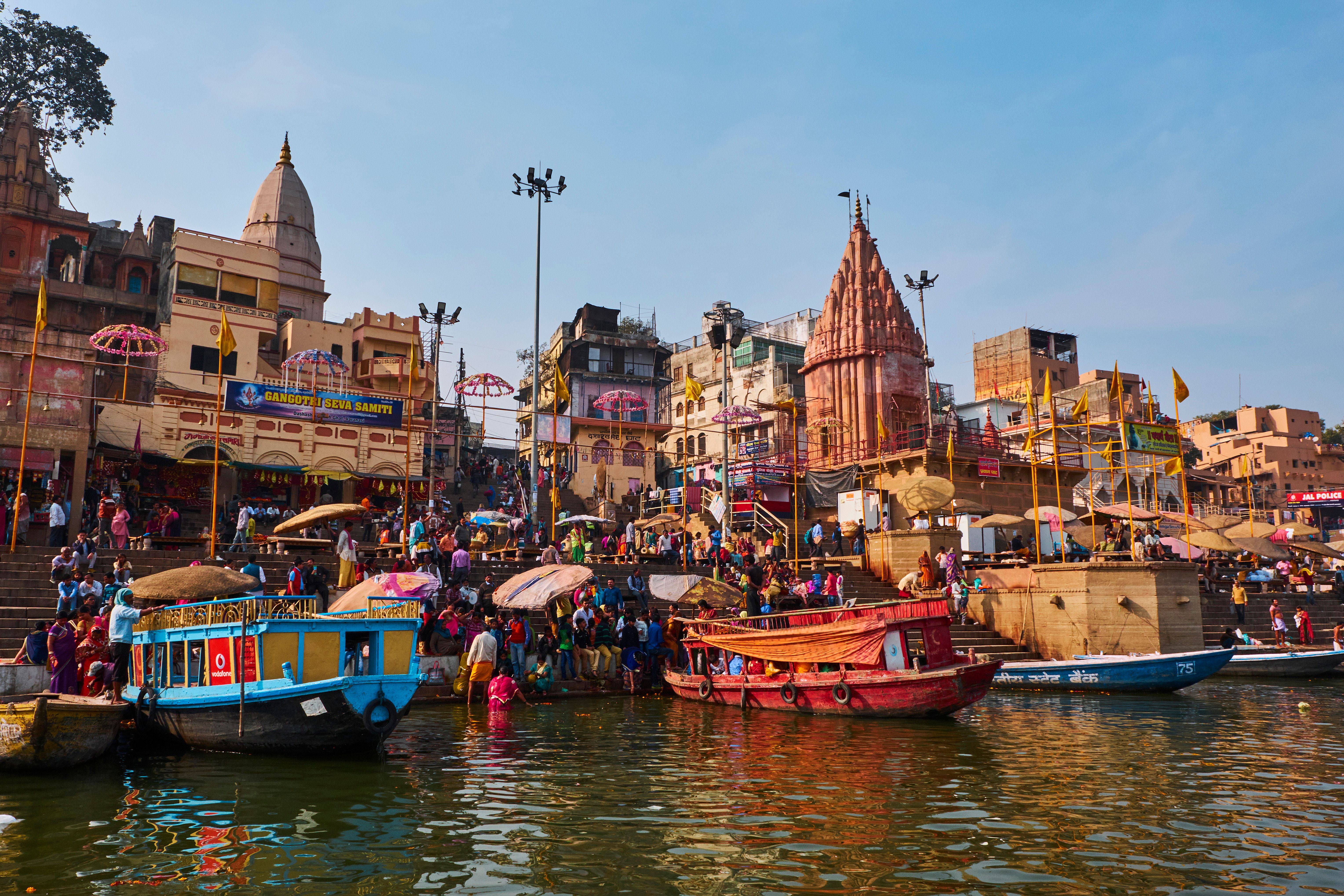 Bunte Boote, viele Menschen und Tempelbauten am Ufer des Ganges in Varanasi, Indien.