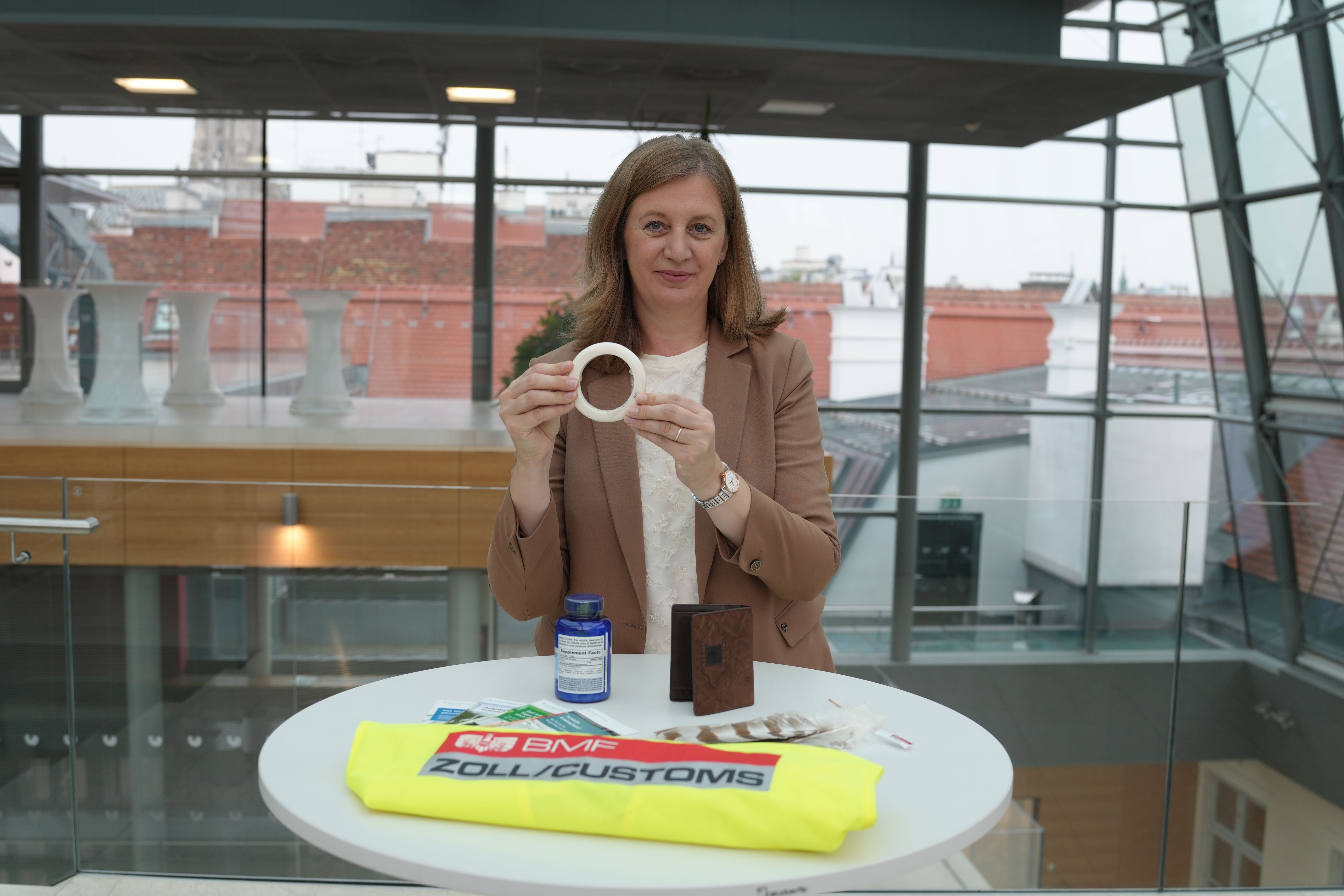Frau hält ein Objekt, Zollartikel liegen auf einem Tisch im modernen Gebäude.