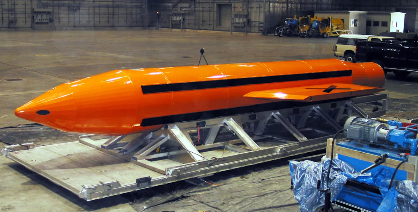 Große orange Bombe mit schwarzen Streifen liegt auf einer Transportplattform in einer Halle.