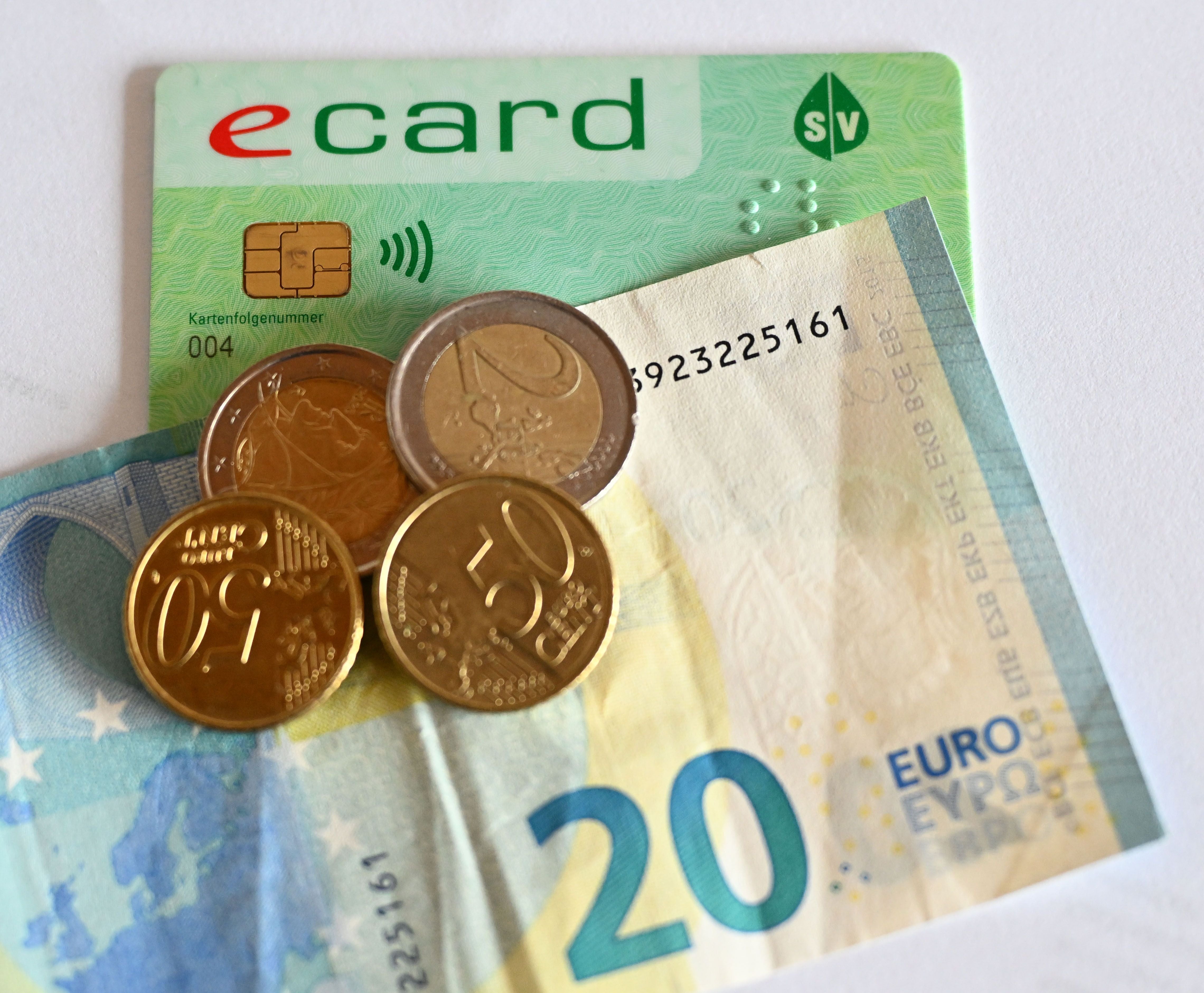 Eine E-Card, ein 20-Euro-Schein und mehrere Euromünzen auf weißem Hintergrund.