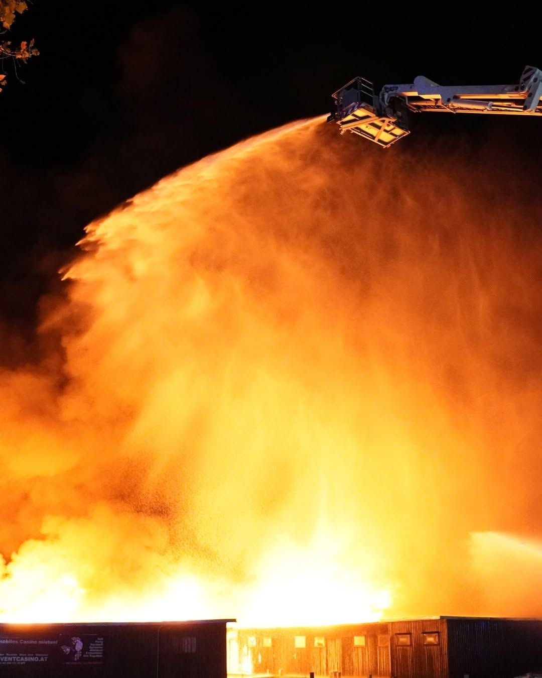 Großbrand bei Nacht, Feuerwehr löscht das Feuer mit Wasser von einer Drehleiter.