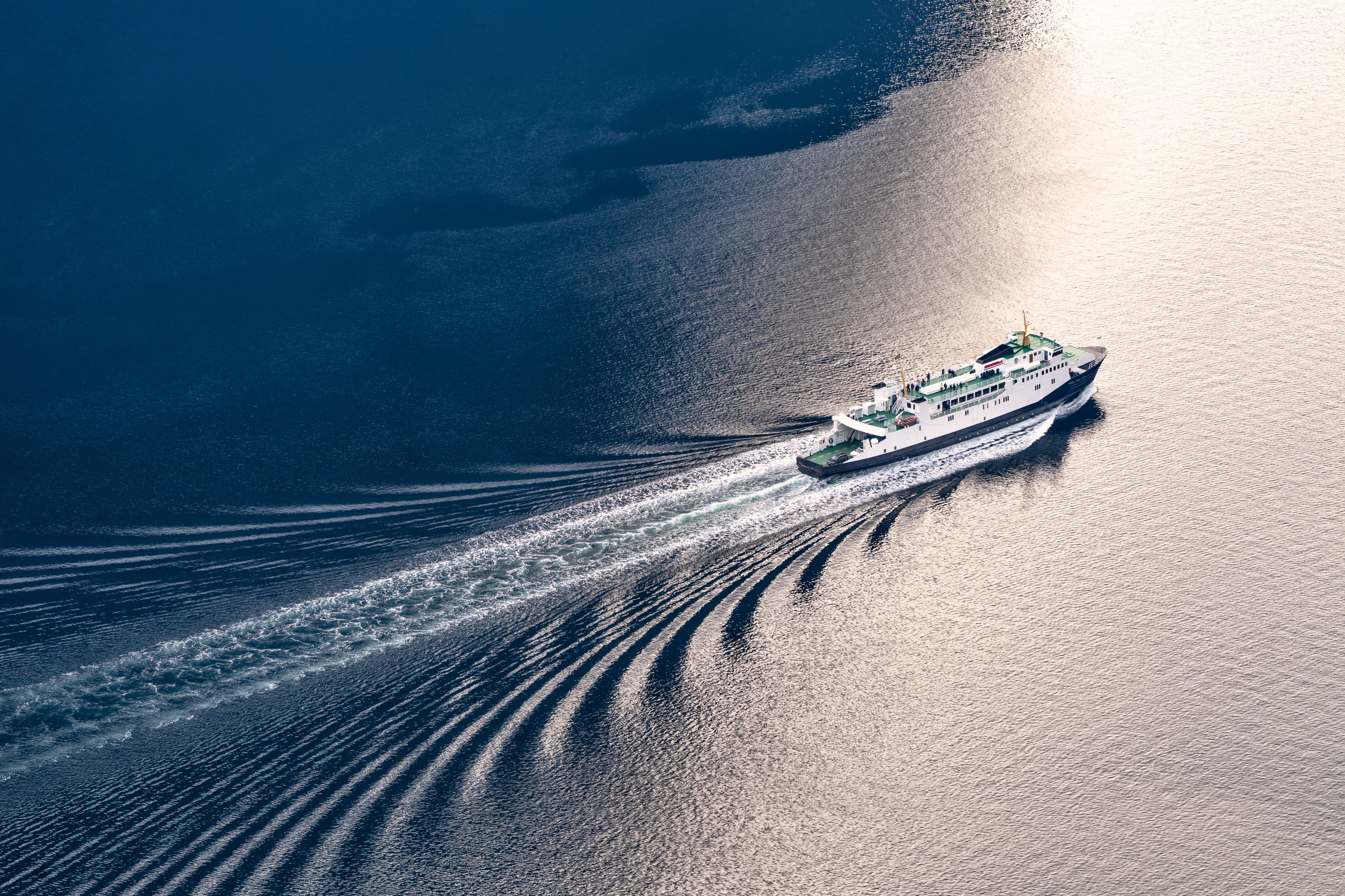 Eine Fähre fährt durch den Geirangerfjord und hinterlässt eine breite Spur im Wasser.
