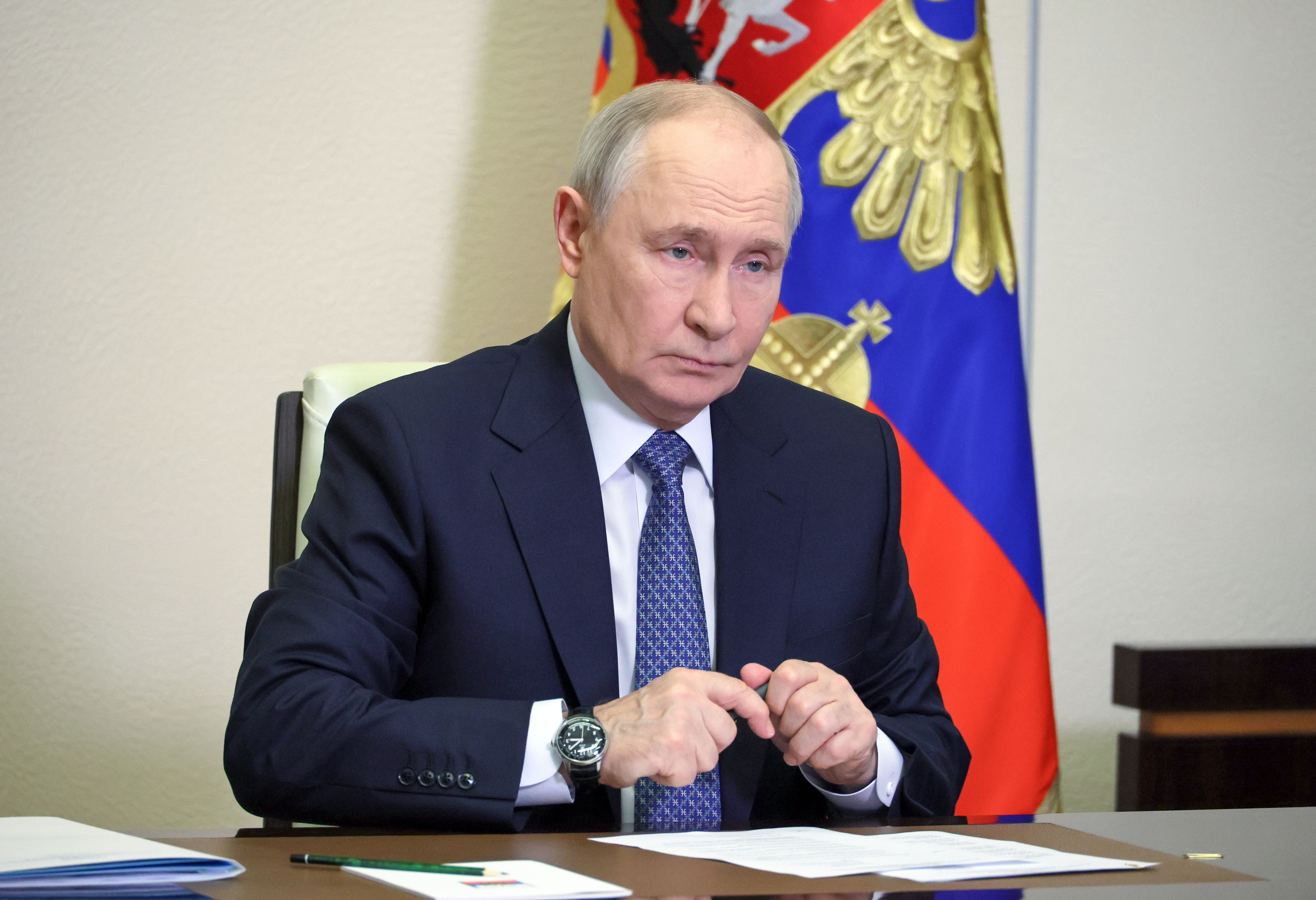 Ein Mann im Anzug sitzt an einem Tisch vor russischer Flagge und Papieren.