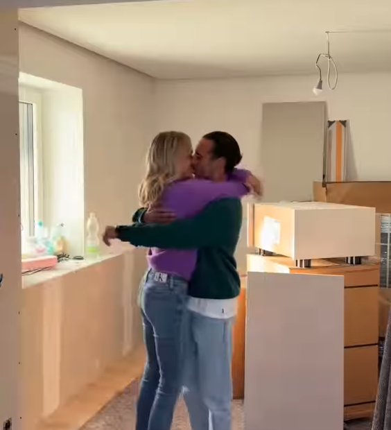 Ein Paar umarmt sich in einem Raum mit Umzugskartons und Möbeln.