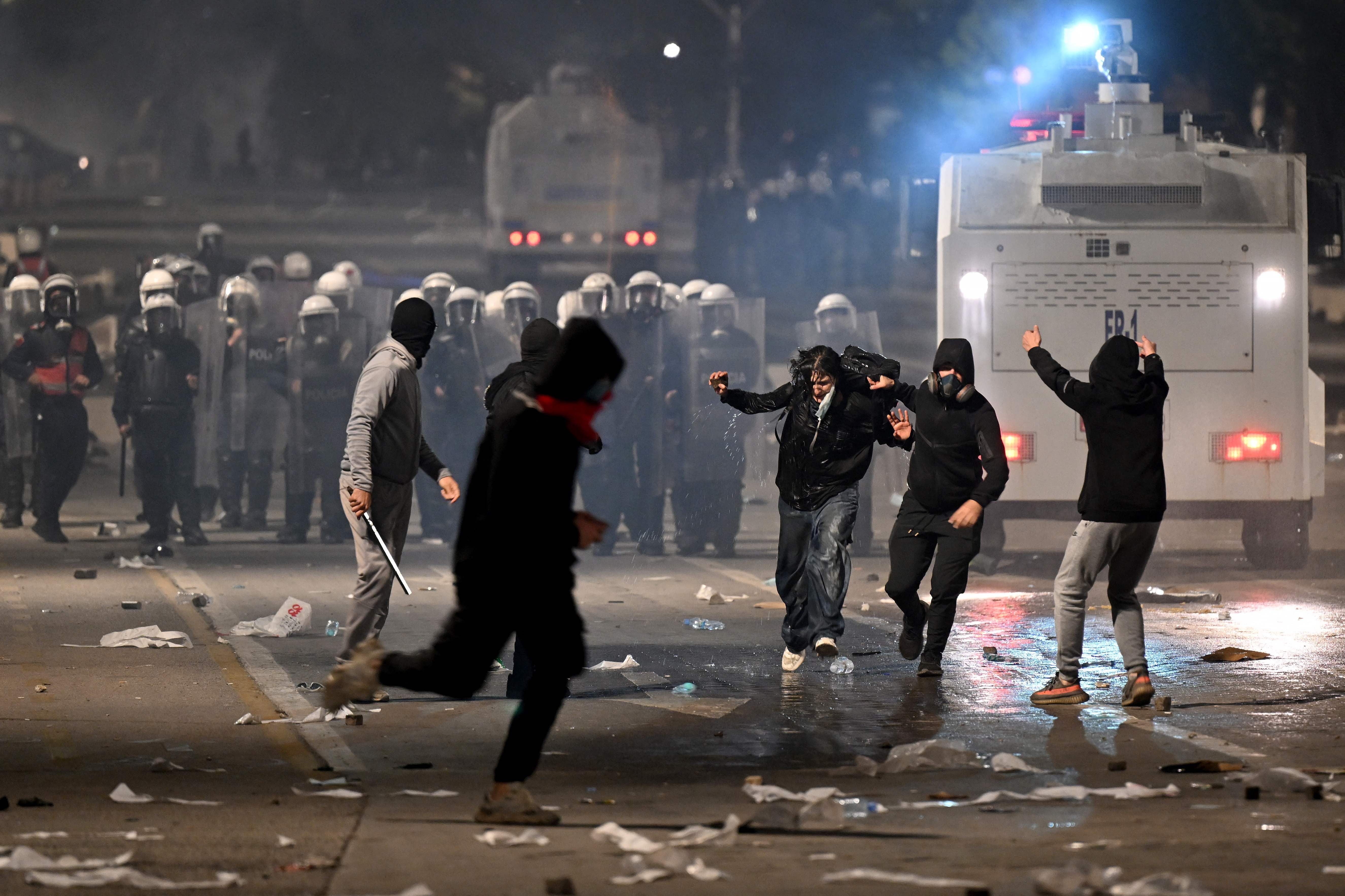 Vermummte Demonstranten stehen Polizisten mit Schilden und Wasserwerfer gegenüber, Müll liegt auf der Straße.