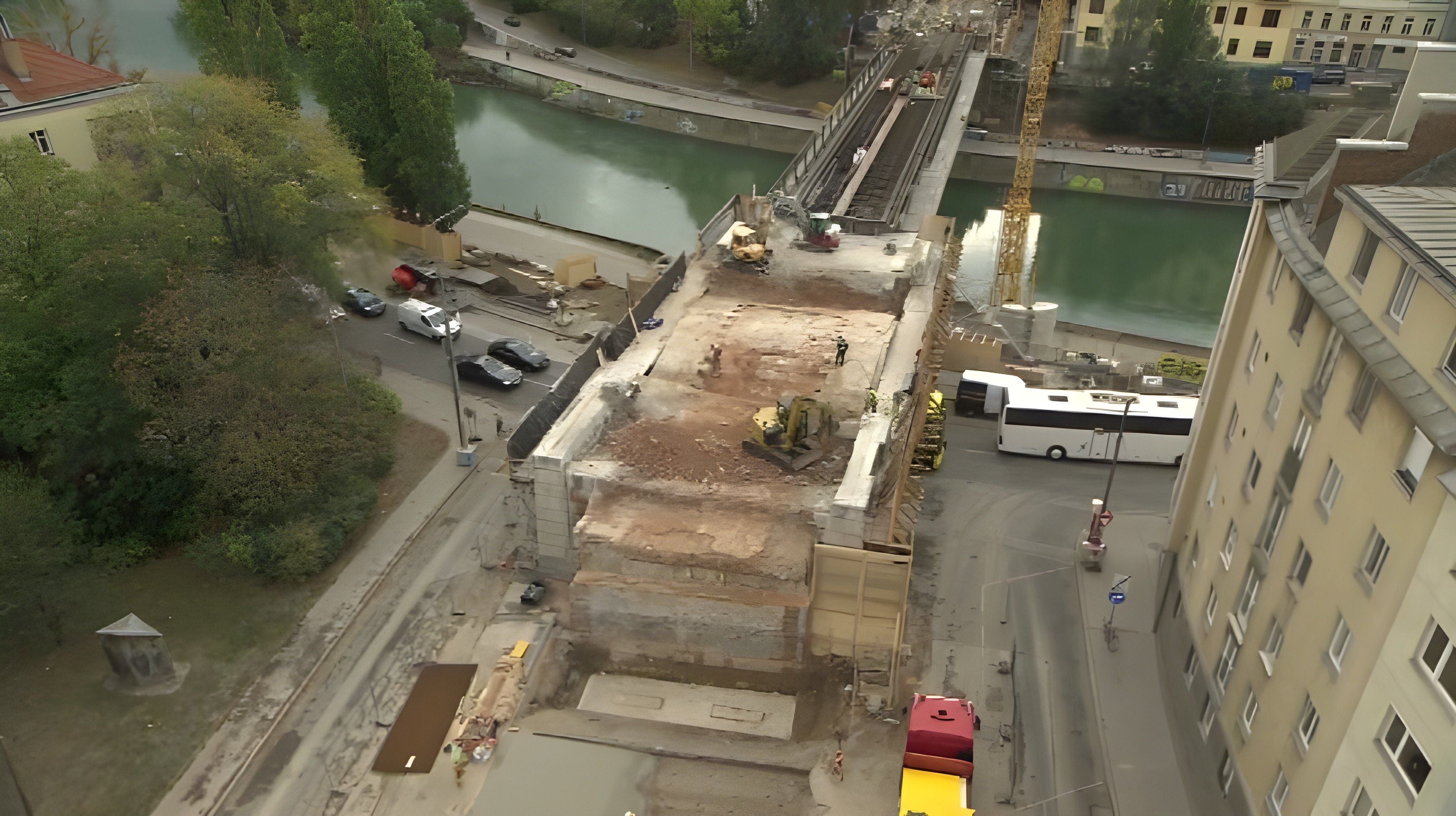 Teilweise abgerissener Viadukt mit Baufahrzeugen zwischen Straße, Fluss und Gebäuden.