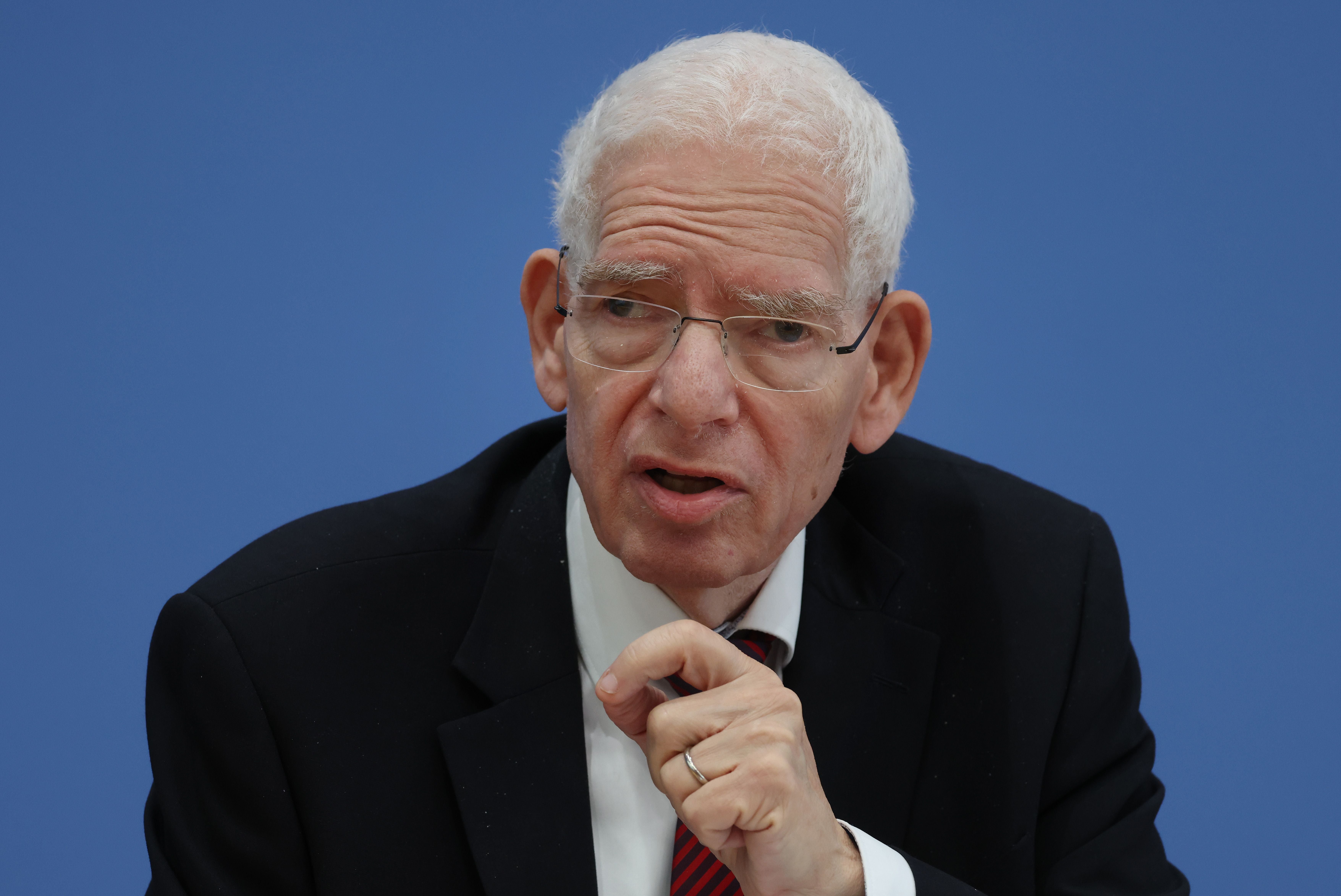 Ein älterer Mann im Anzug spricht vor blauem Hintergrund in ein Mikrofon.