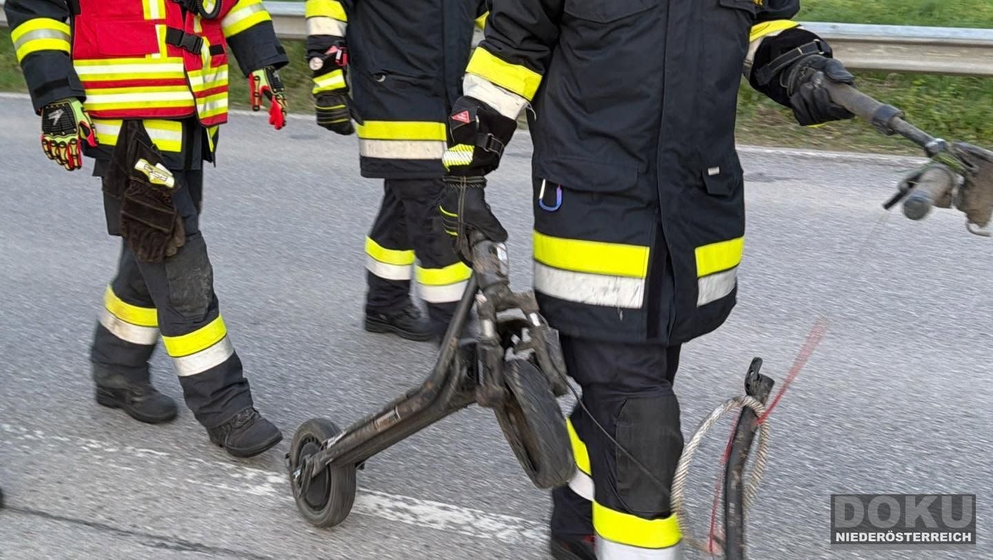 Feuerwehrleute tragen ein beschädigtes E-Scooter-Teil auf einer Straße.