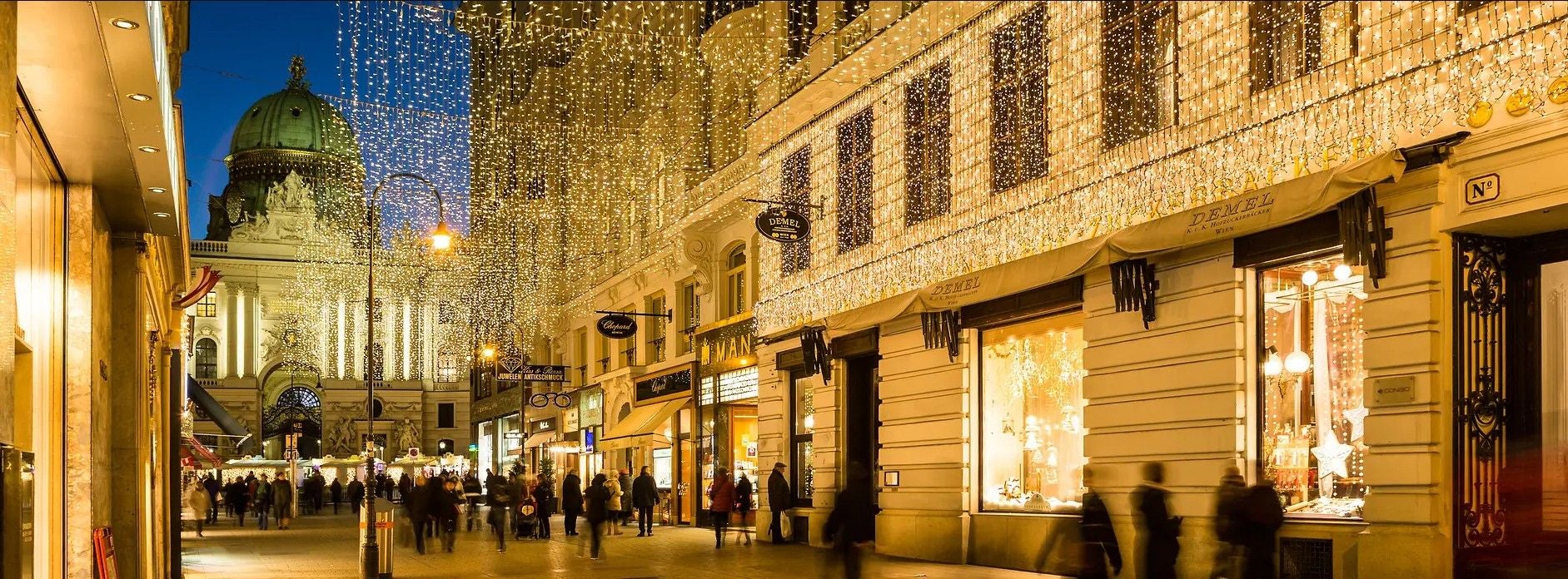 Menschen spazieren unter festlicher Weihnachtsbeleuchtung in Wiens historischer Innenstadt.