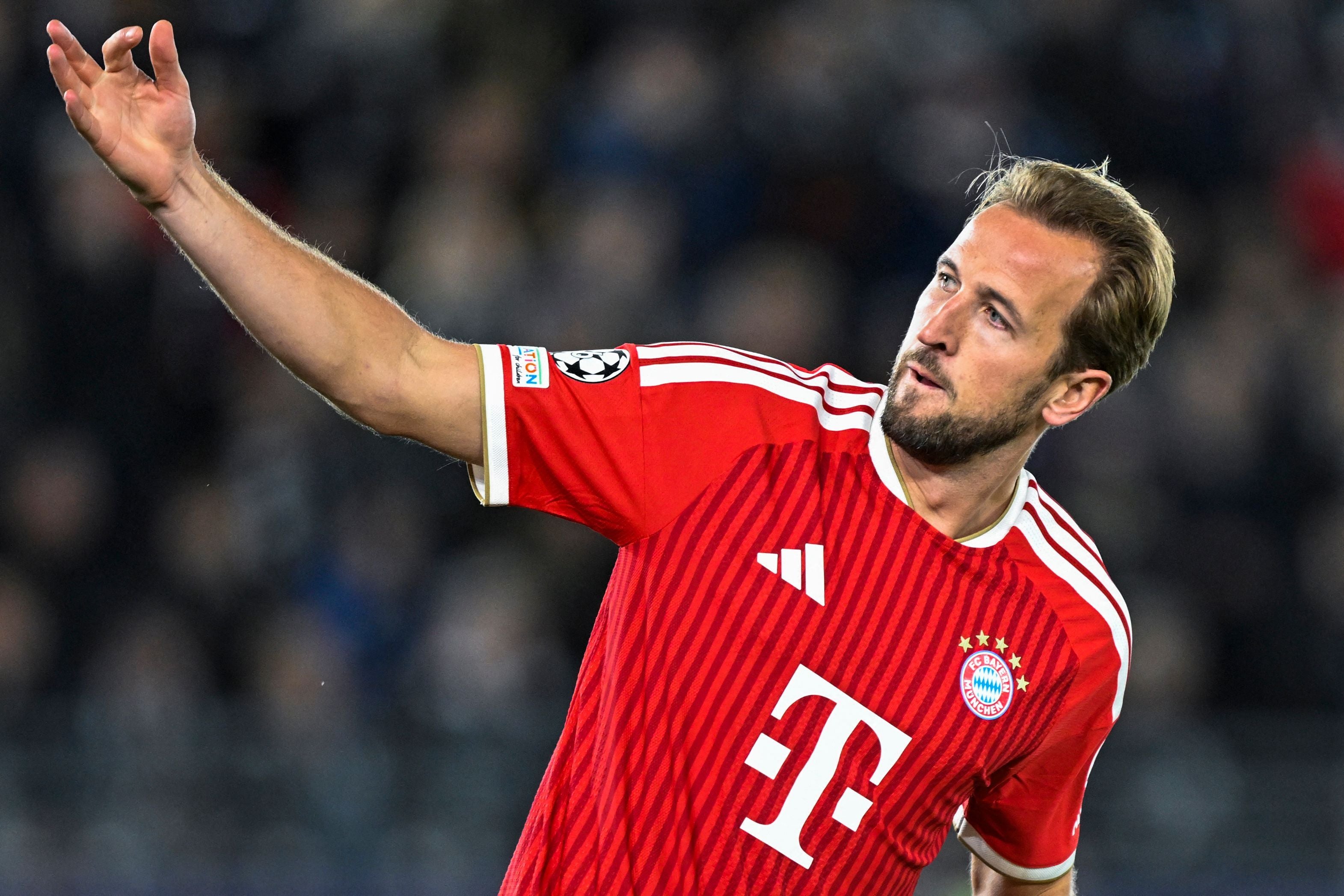 Harry Kane vom FC Bayern München im rot-gestreiften Trikot streckt auf dem Spielfeld den rechten Arm nach oben und blickt aufmerksam zur Seite.