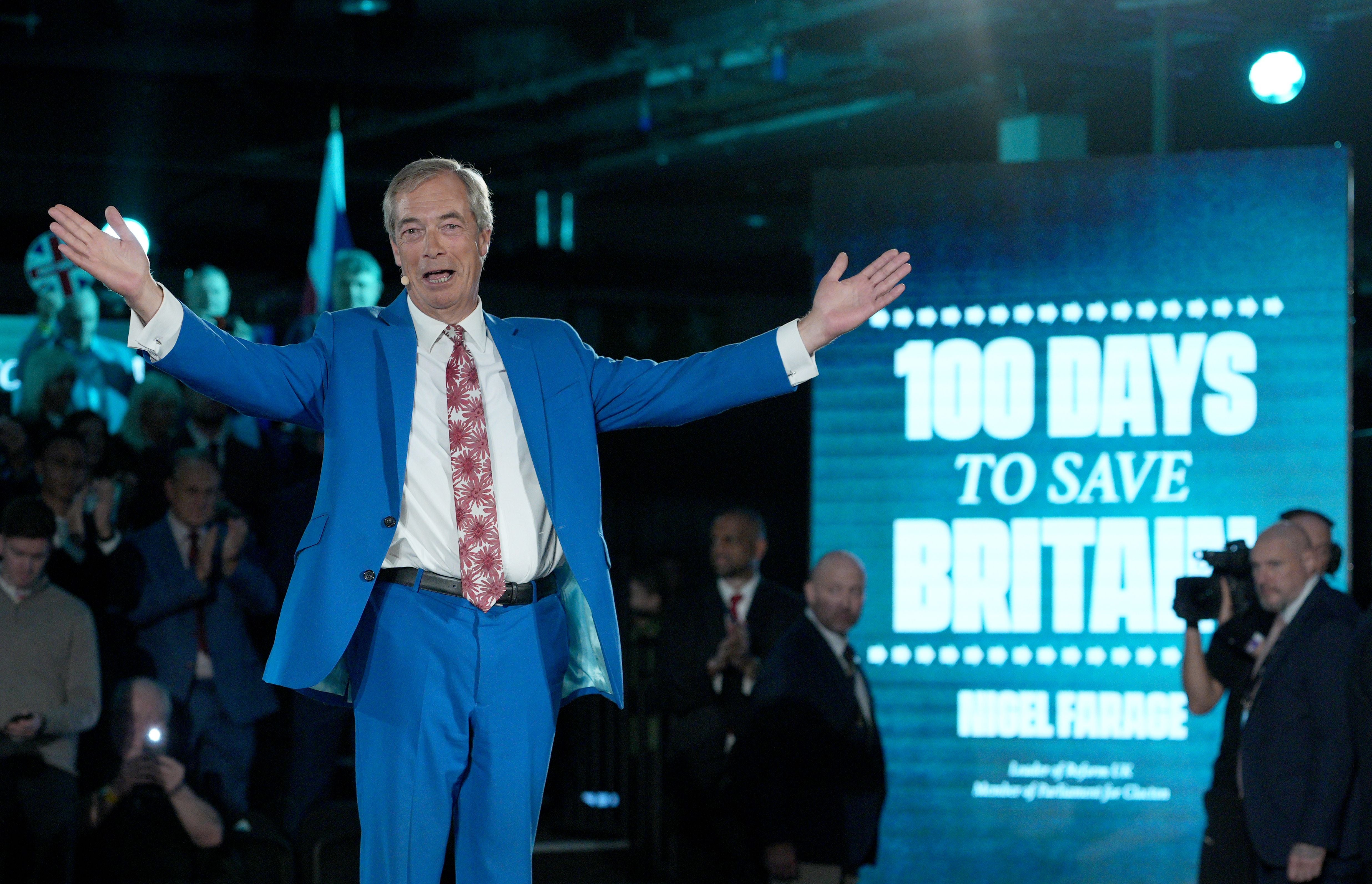 Ein Mann im blauen Anzug spricht auf einer Bühne, hinter ihm steht „100 Days to Save Britain“.