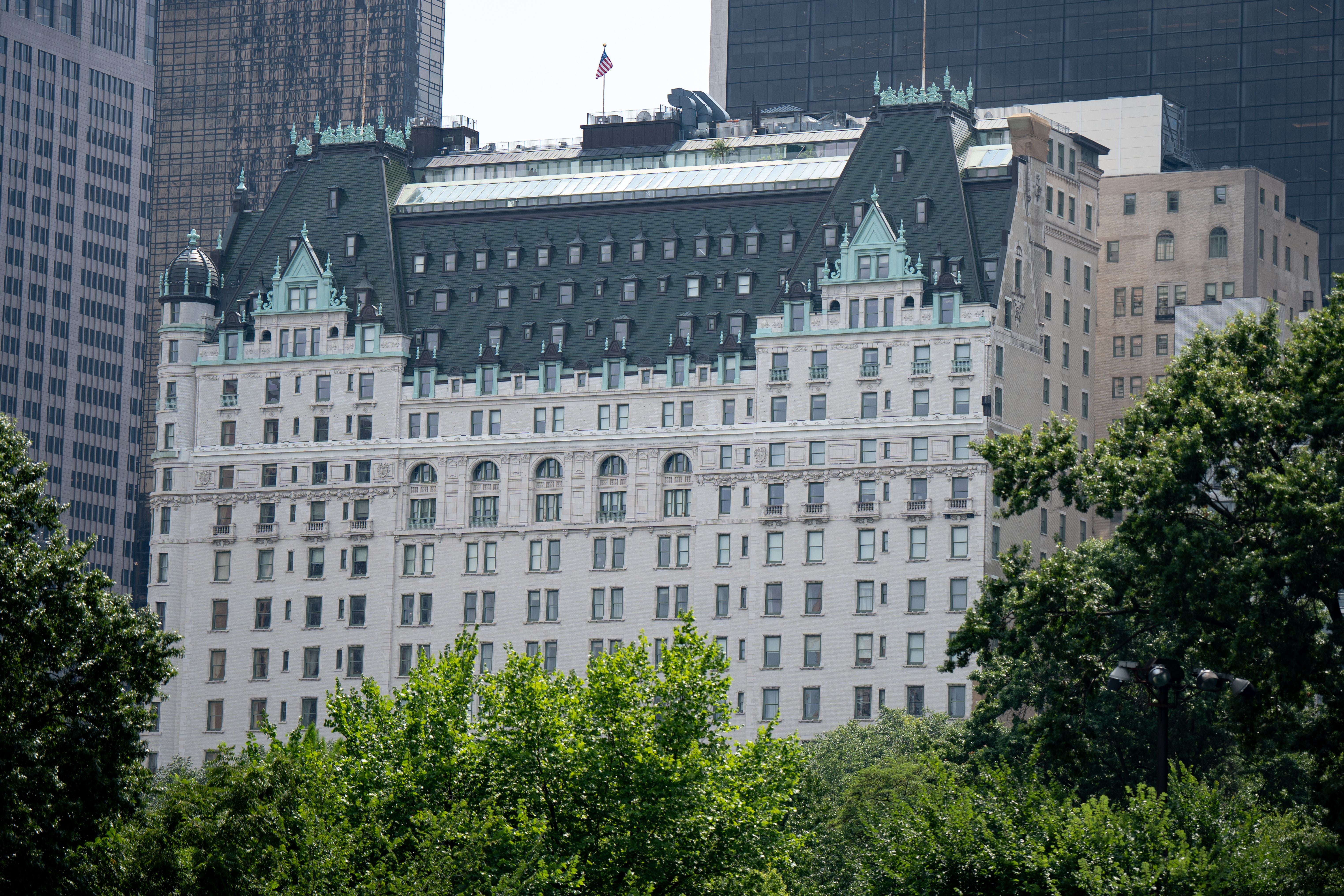 Das Plaza Hotel in New York City mit grünen Bäumen im Vordergrund und Hochhäusern im Hintergrund.