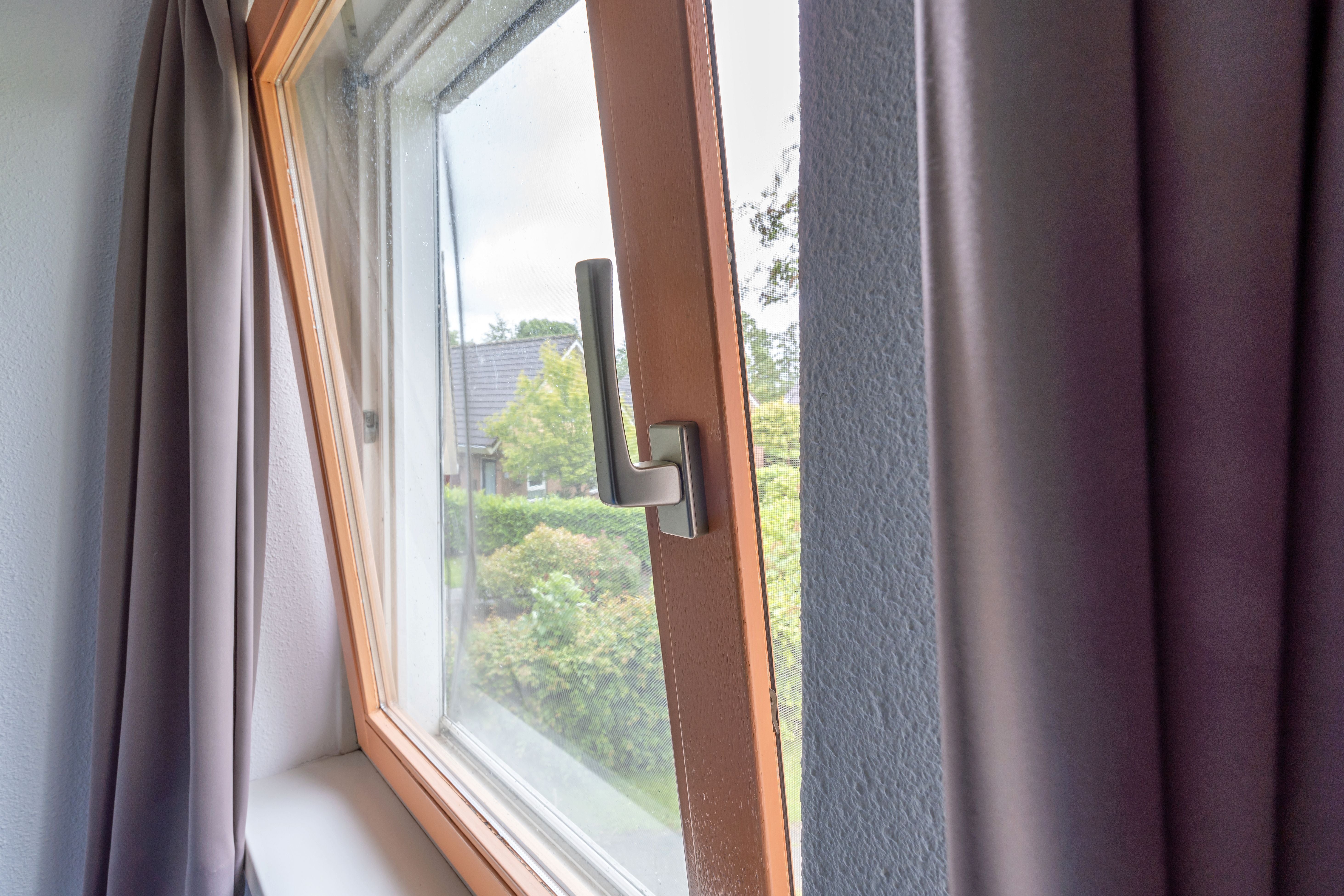 Gekipptes Fenster in einem Wohngebäude mit Blick auf Garten und Nachbarhaus.