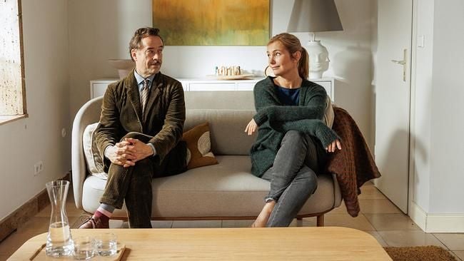 Ein Mann und eine Frau sitzen distanziert auf einem Sofa in einem modern eingerichteten Raum.