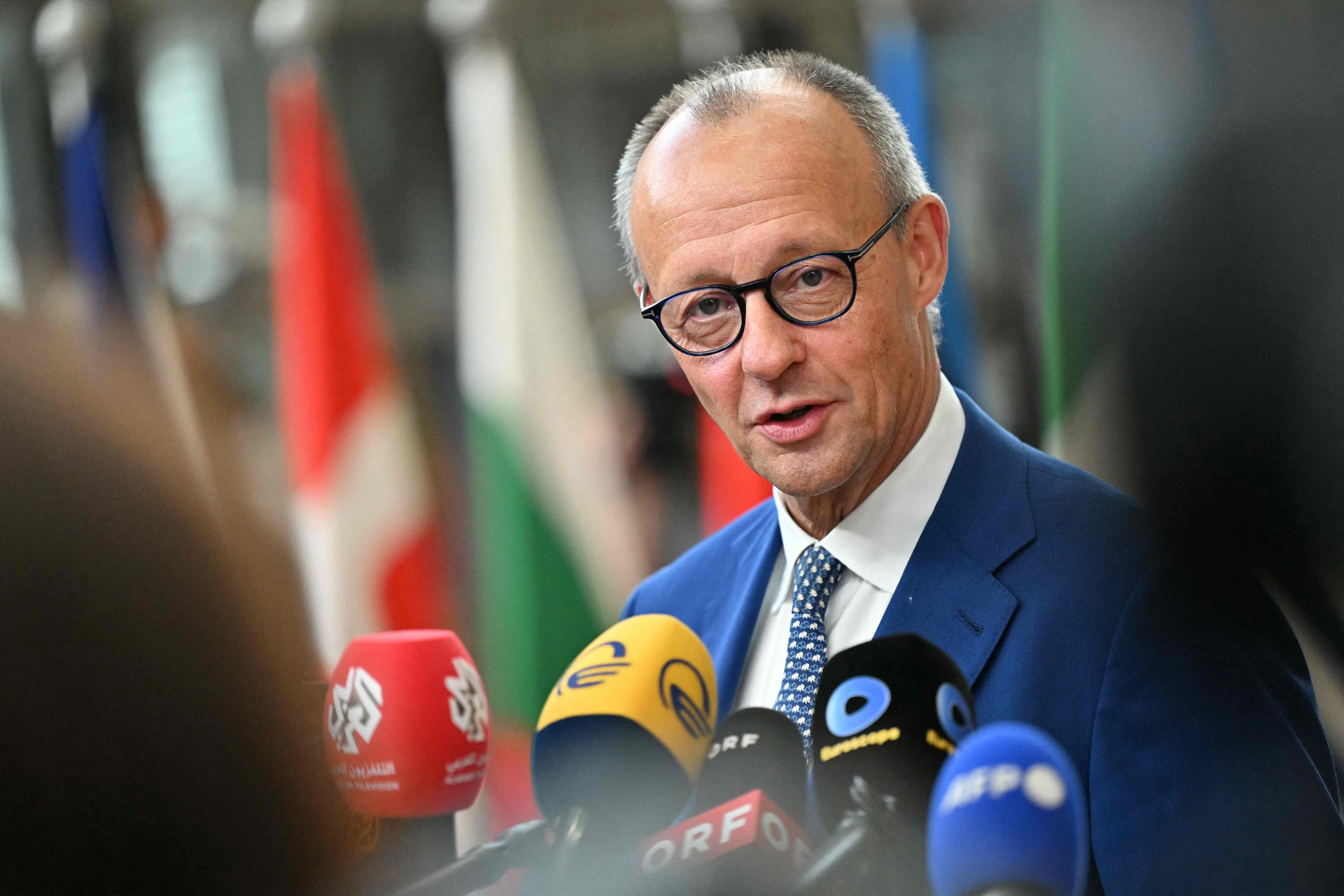 Ein Mann im blauen Anzug spricht vor mehreren Mikrofonen auf einer Pressekonferenz.