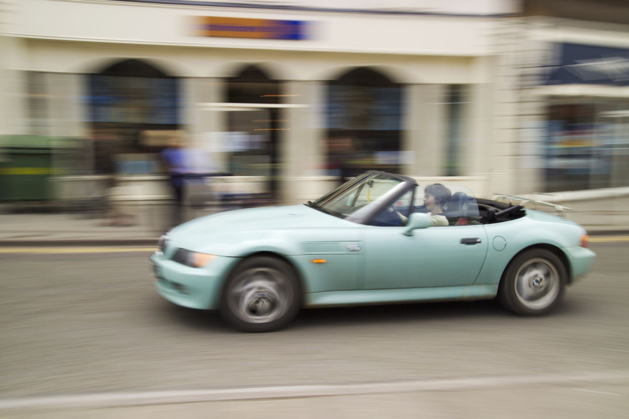 Ein hellblauer BMW Cabrio fährt schnell durch eine Stadtstraße.