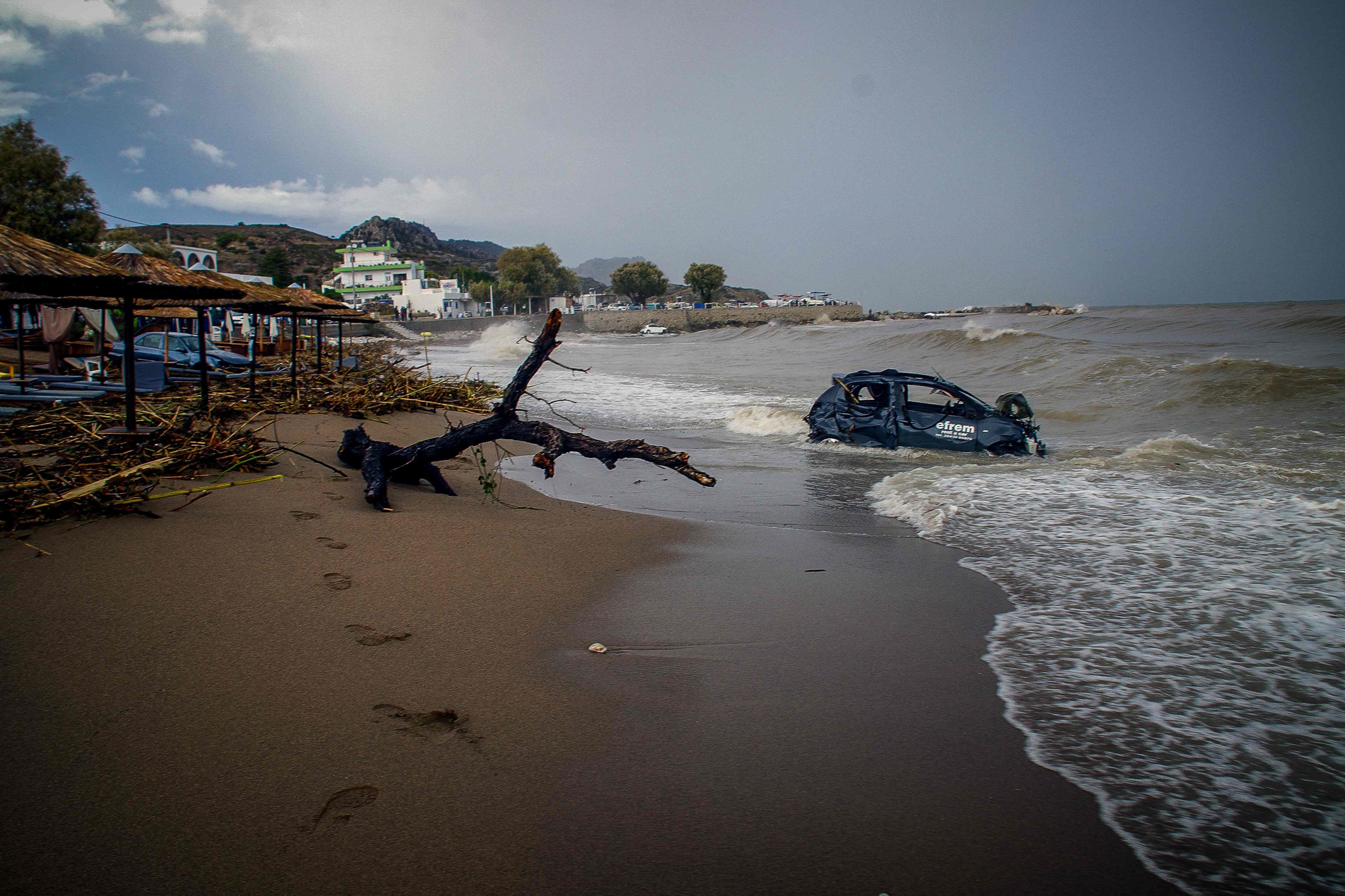 Ein zerstörtes Auto liegt nach Überschwemmungen teils im Meer an einem verlassenen Strand.