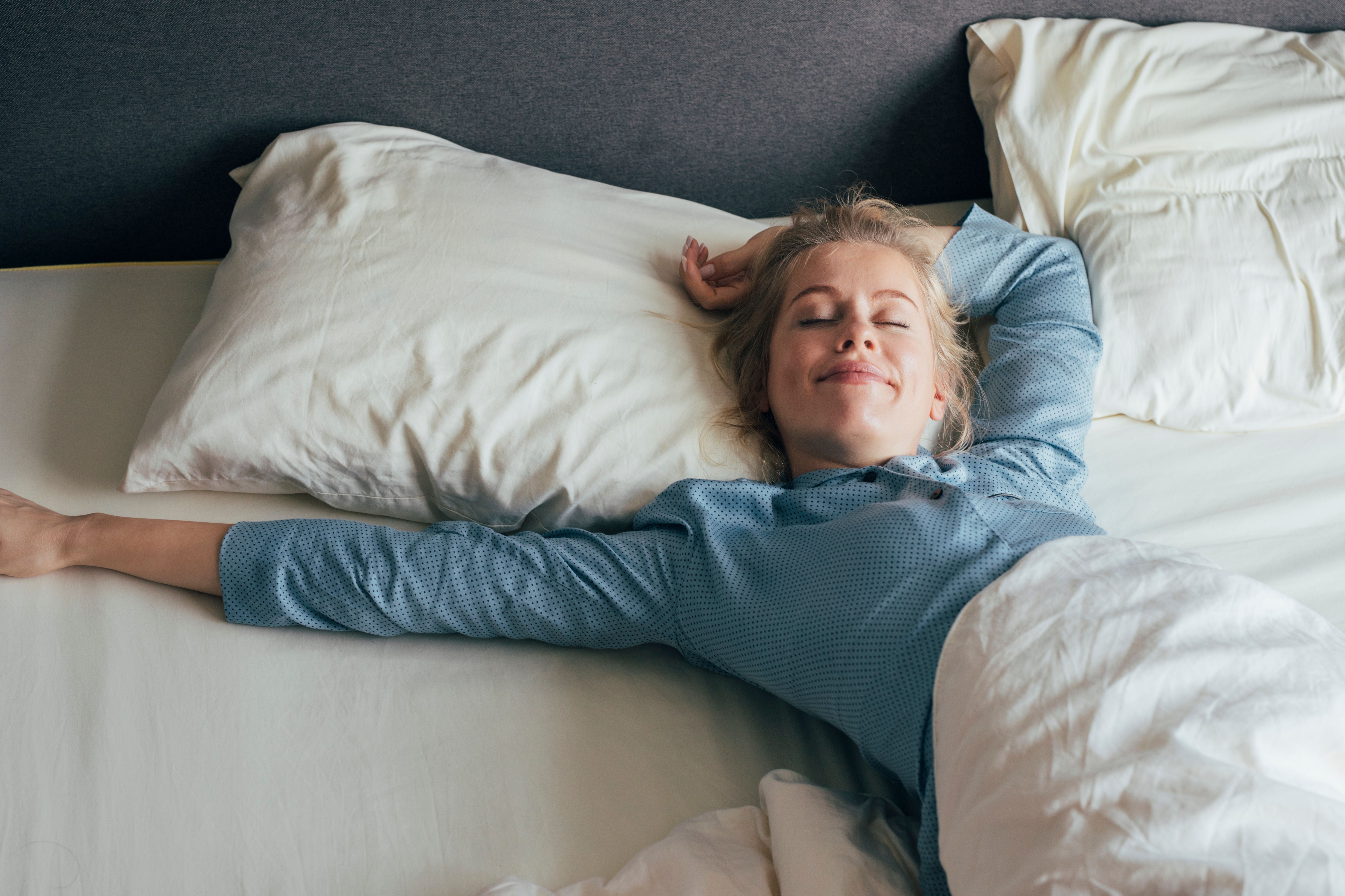 Junge Frau liegt lächelnd im Bett und streckt sich entspannt am Morgen.
