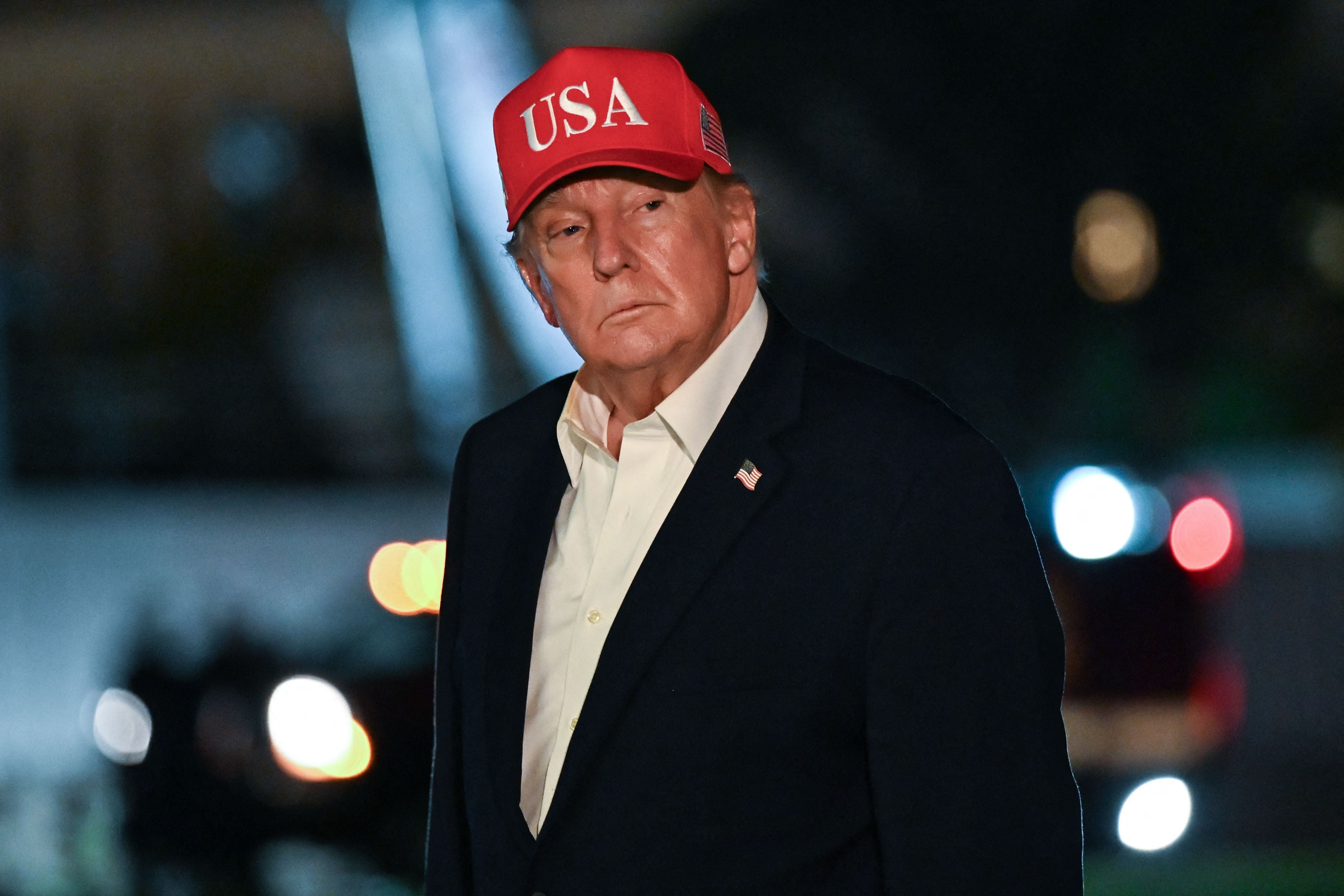 Mann mit roter "USA"-Kappe und dunklem Blazer bei Nacht im Freien.