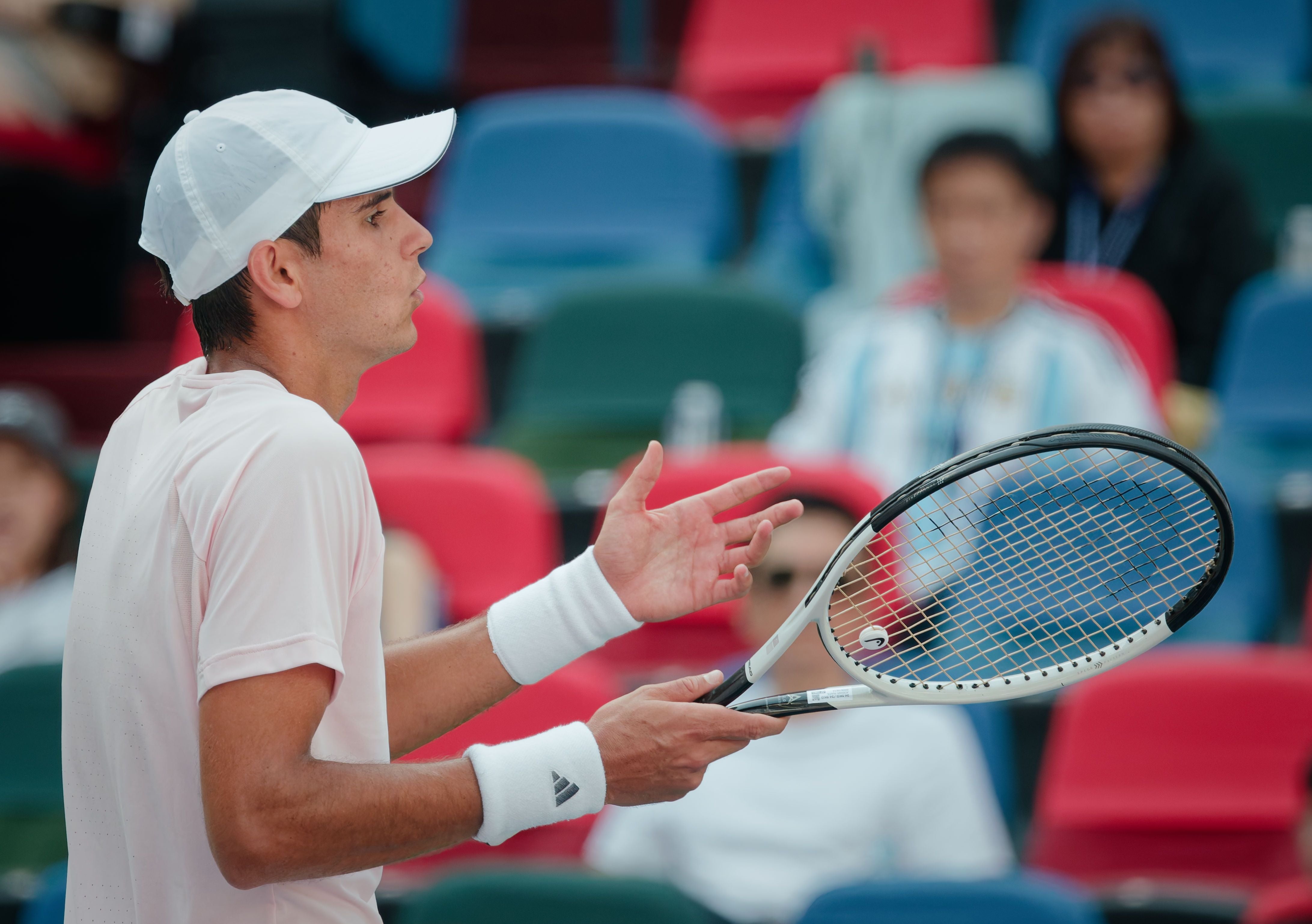 Ein Tennisspieler gestikuliert auf dem Platz, Zuschauer sitzen im Hintergrund.