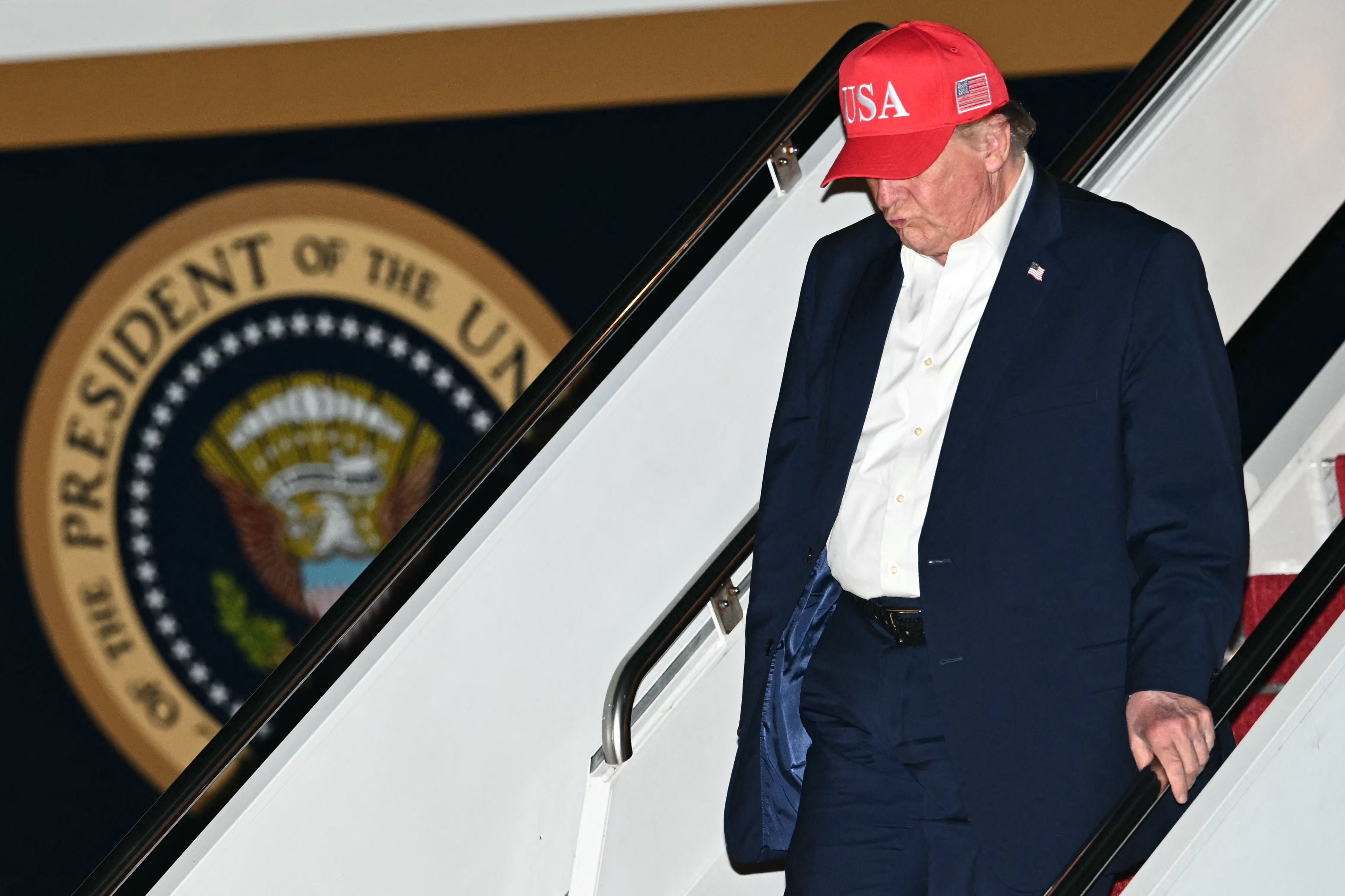 Ein Mann mit roter "USA"-Kappe steigt nachts die Flugzeugtreppe vor Präsidentensiegel hinab.