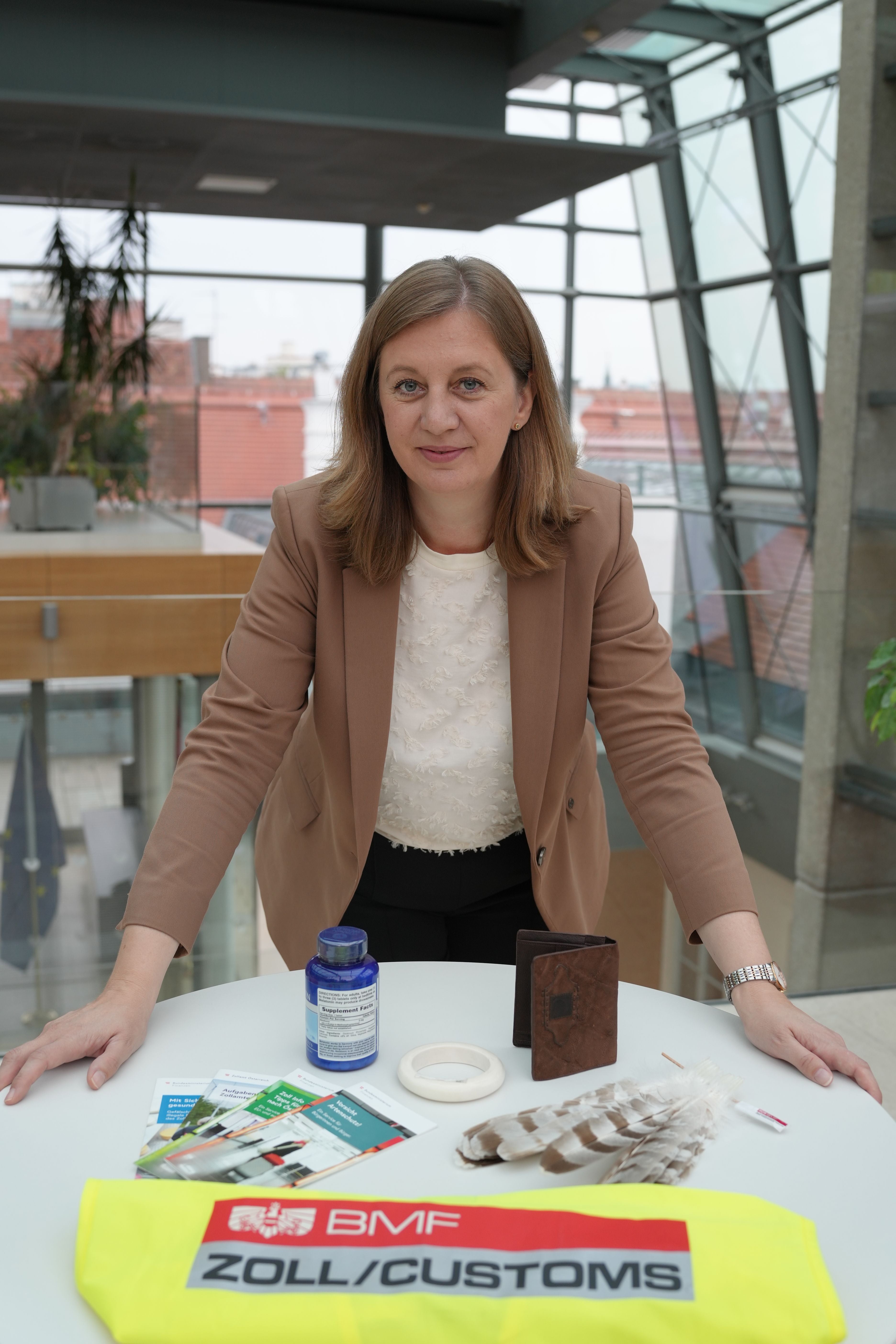 Frau steht an einem Tisch mit Zollutensilien wie Federn, Pässen und einer Zollweste.
