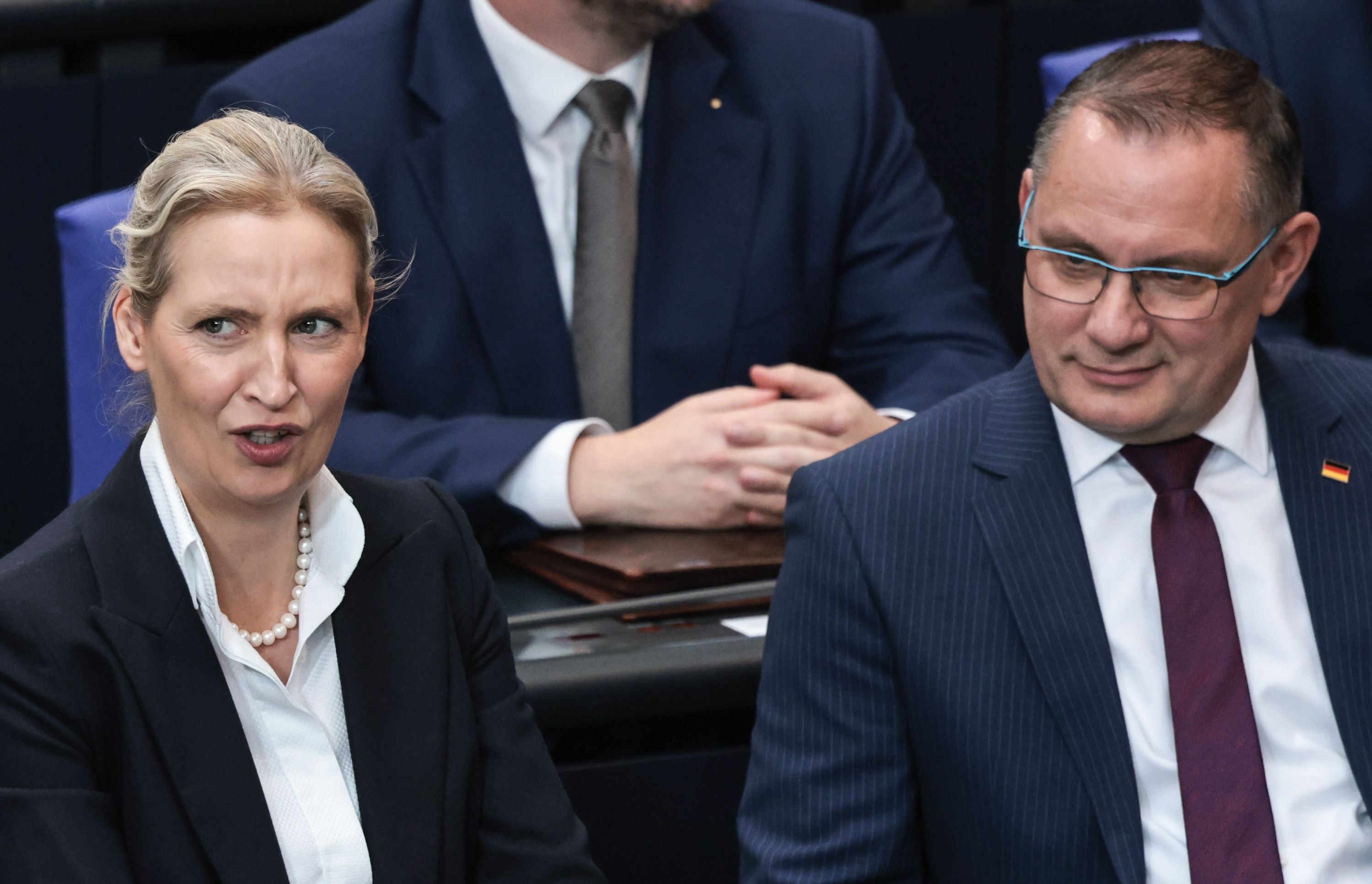 Zwei Personen im Anzug sitzen nebeneinander im Bundestag und unterhalten sich.