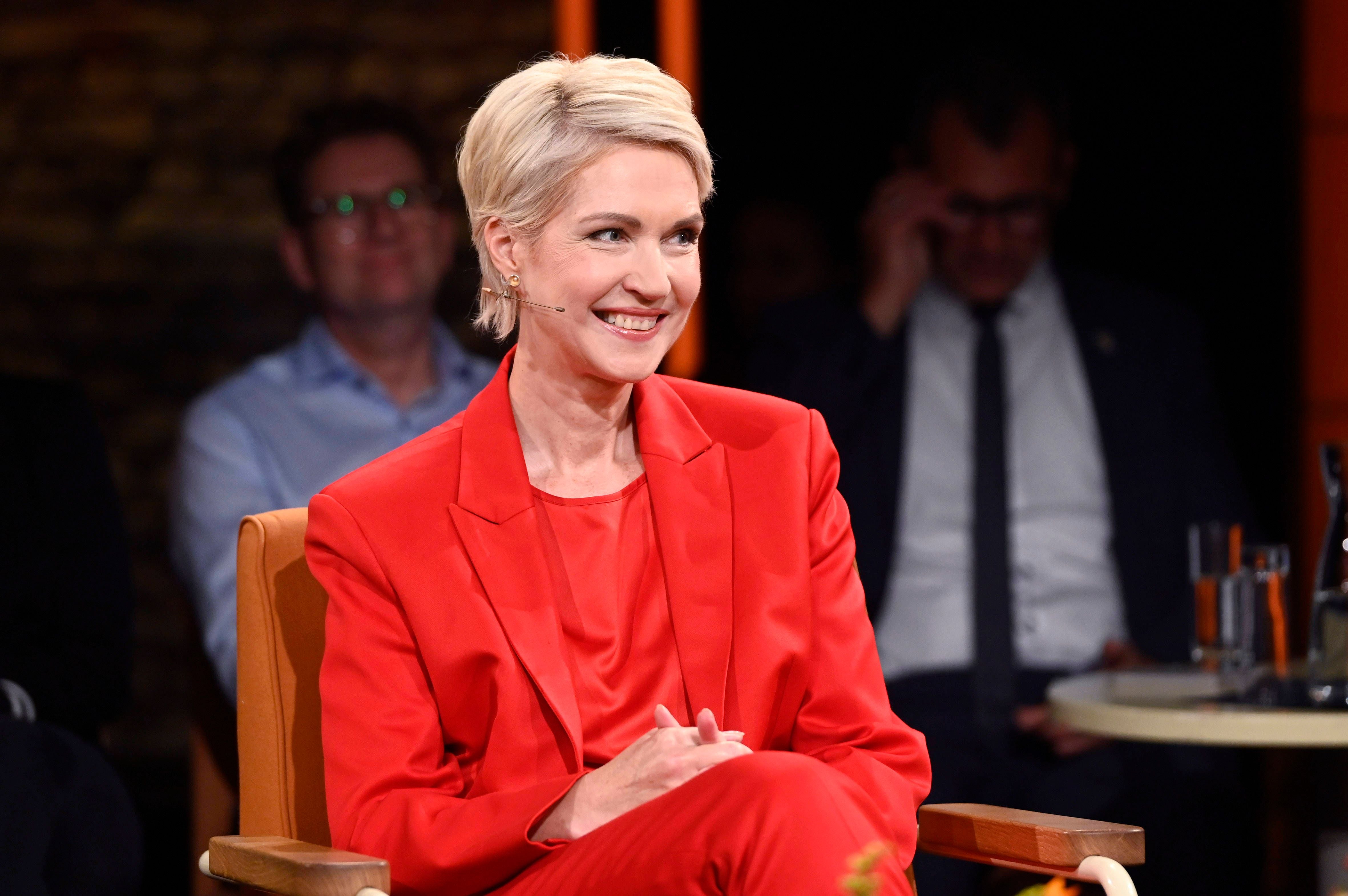 Frau im roten Anzug lächelt während einer Talkshow-Aufzeichnung im Studio.