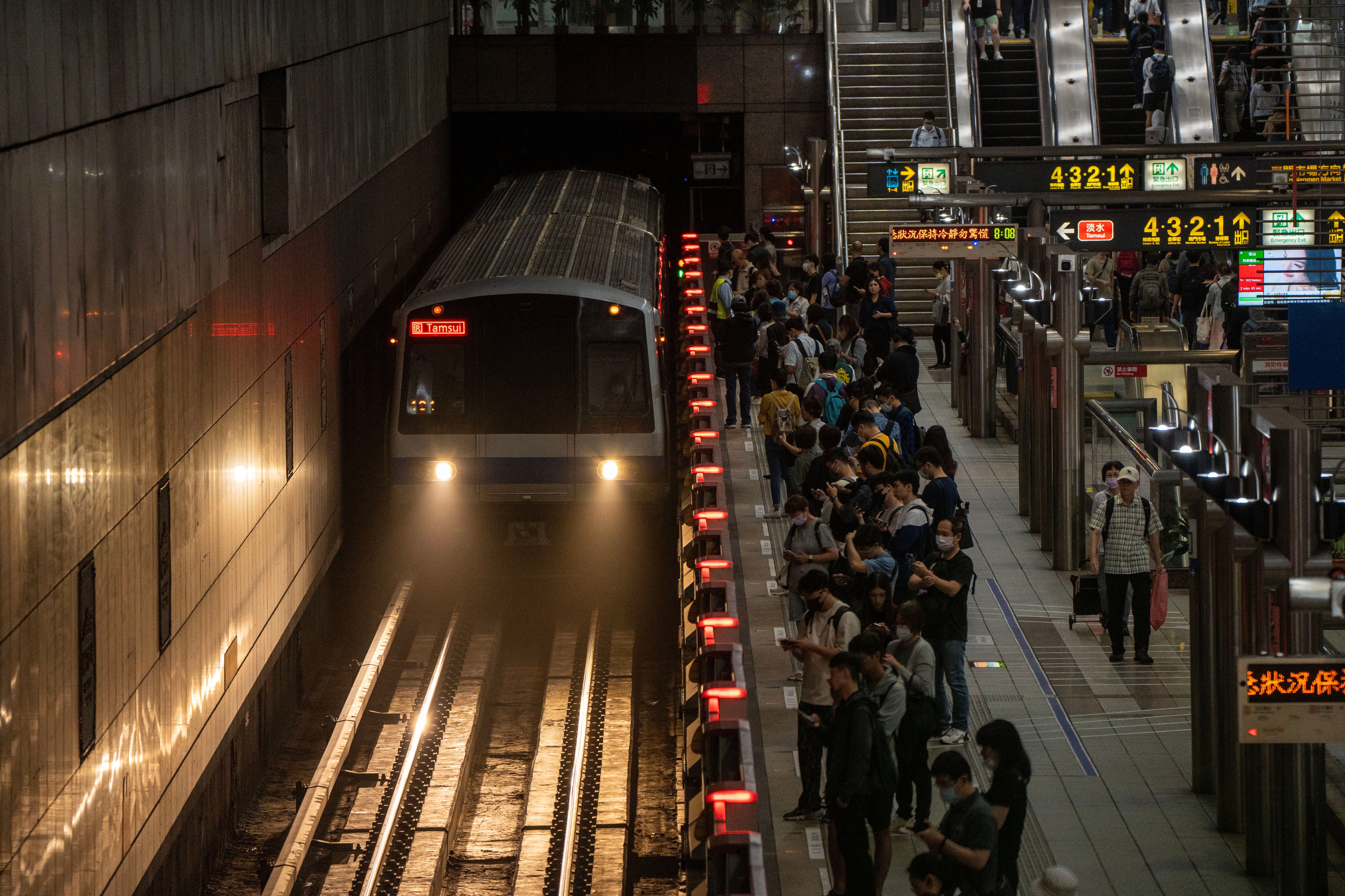 Eine Metro fährt in einen vollen Bahnhof in Taipei ein, viele Menschen warten am Bahnsteig.
