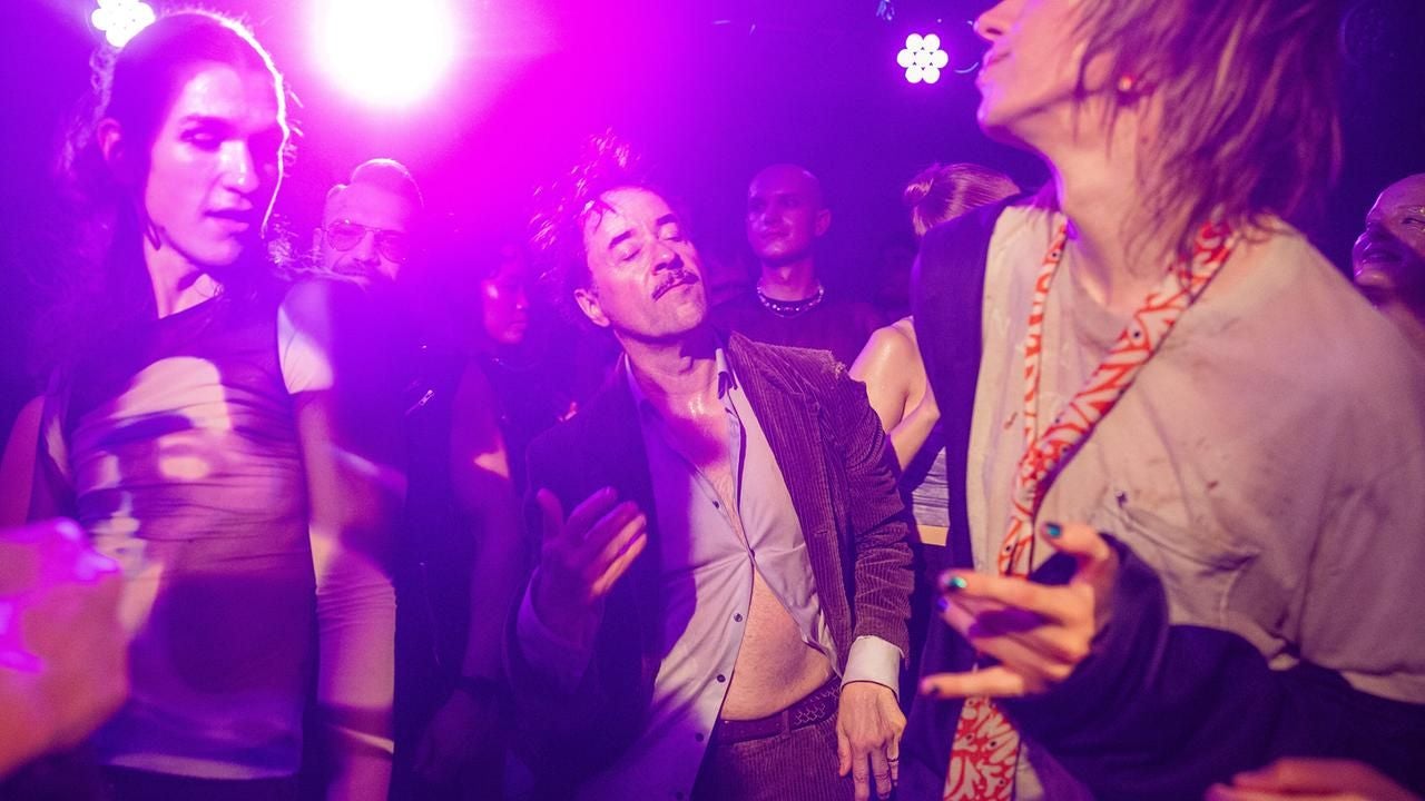 Mehrere Menschen tanzen ausgelassen in lila und gelbem Partylicht.