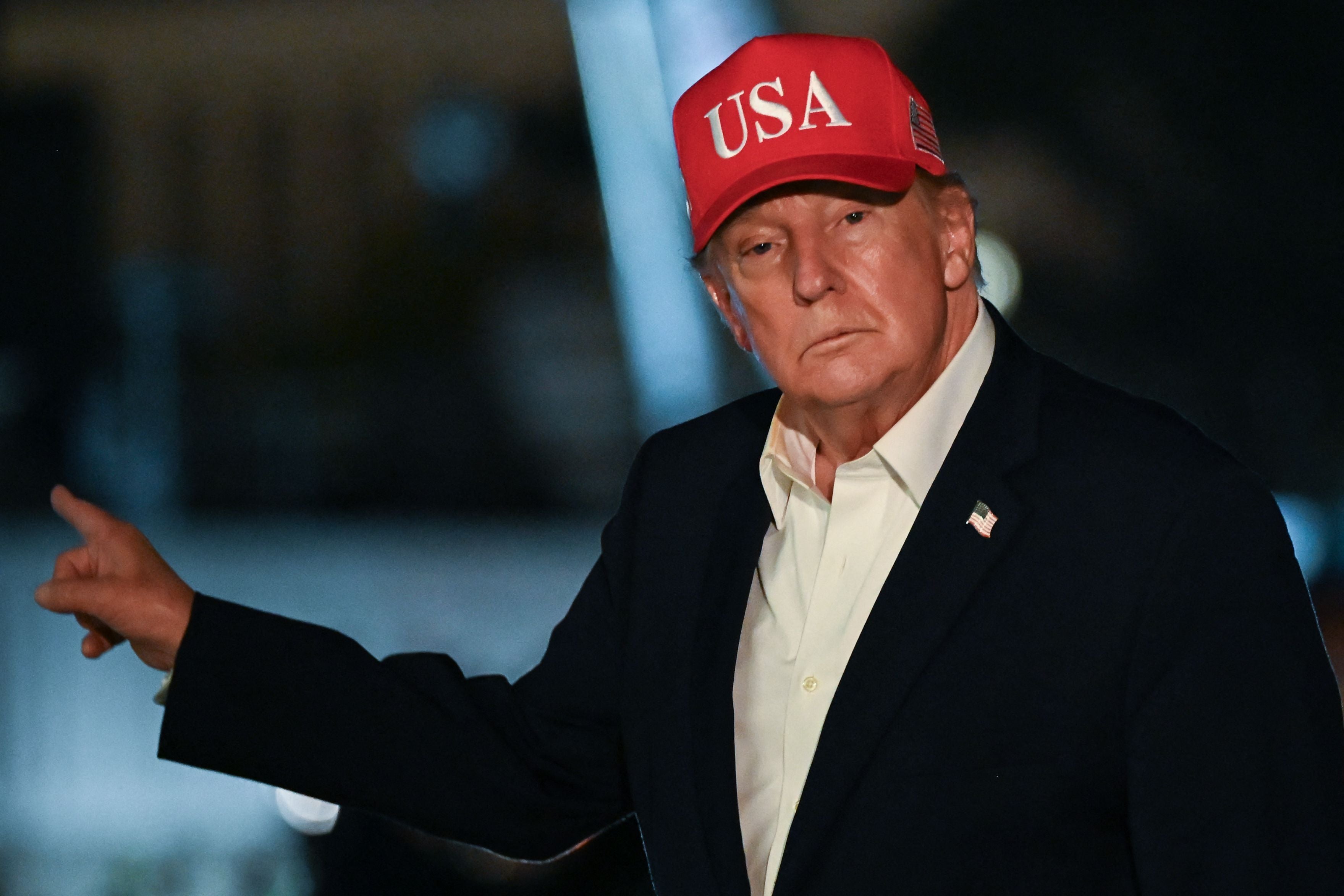 Ein Mann mit roter "USA"-Kappe und dunklem Sakko zeigt mit dem Finger zur Seite.