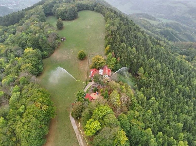 Luftaufnahme von Feuerwehrübung im Wald mit Wasserschläuchen und rotem Gebäude am Geisbühel.