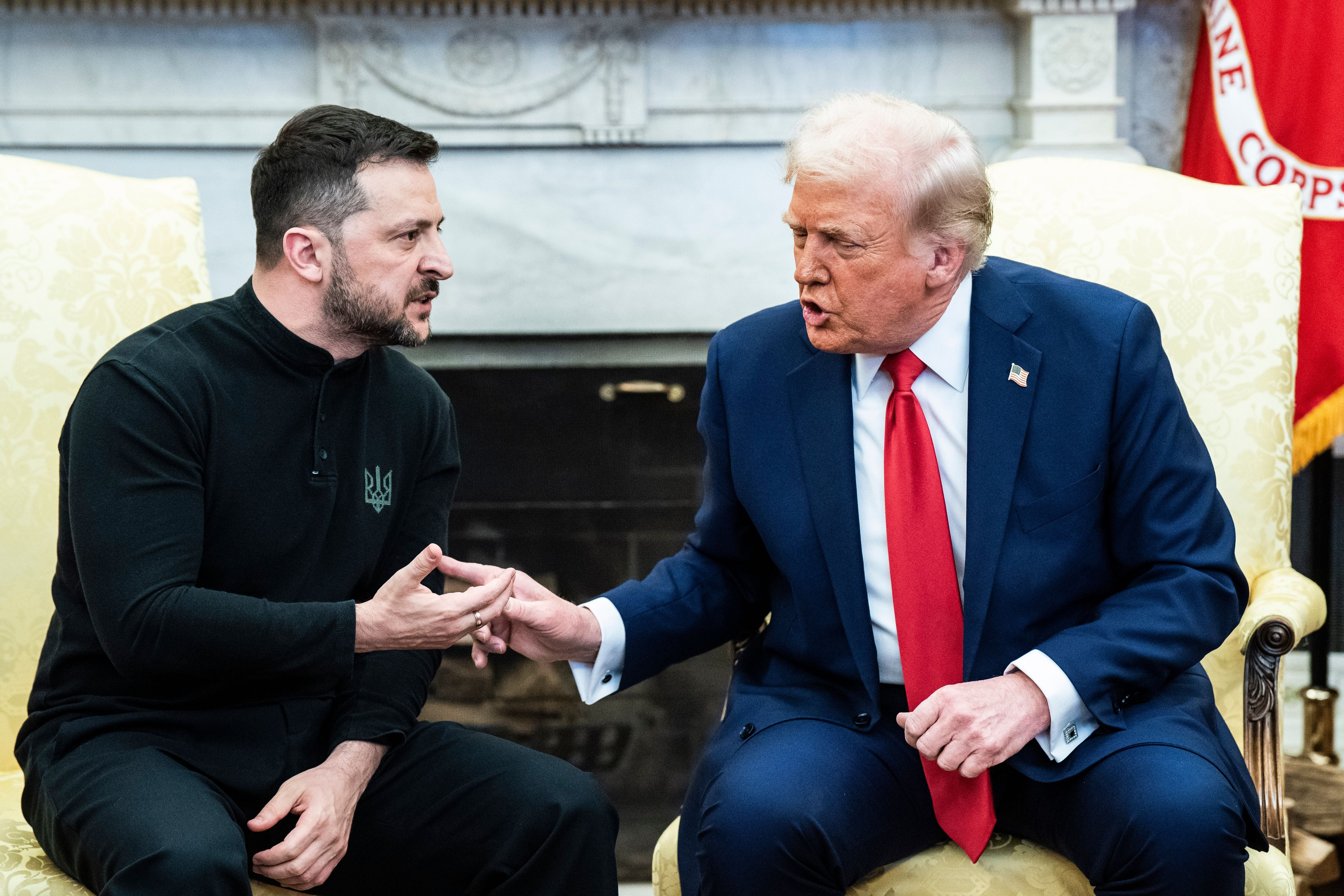 Zwei Männer sitzen diskutierend nebeneinander in einem eleganten Raum mit Kamin im Hintergrund.
