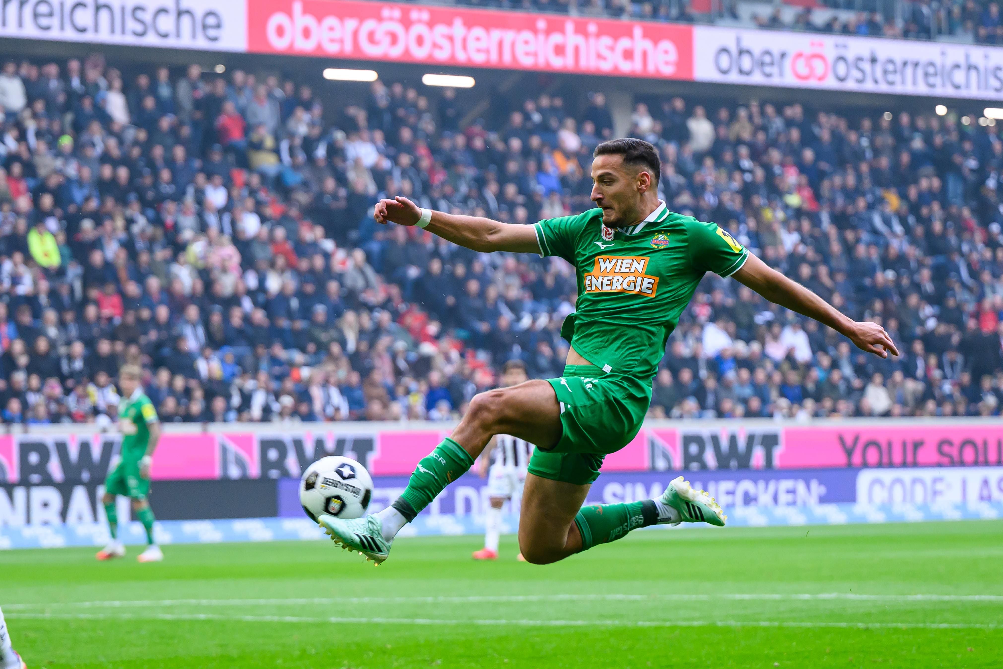 Ein Fußballspieler von Rapid Wien springt und schießt den Ball während eines Spiels im Stadion.