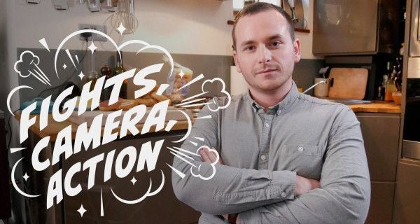 Ein Mann steht mit verschränkten Armen in einer Küche, Schriftzug „Fights, Camera, Action“.