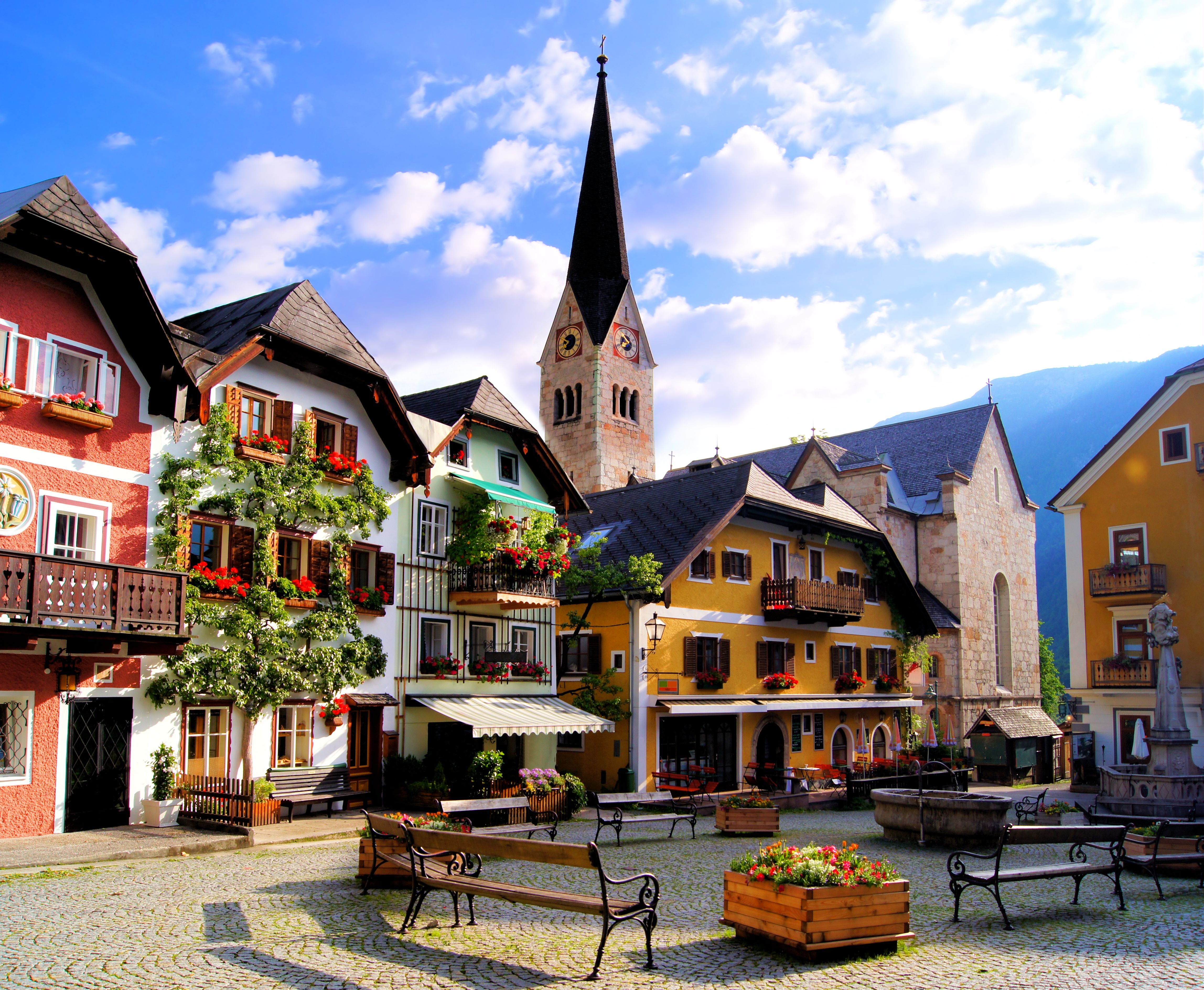 Bunte Häuser und Kirche an einem idyllischen Platz im österreichischen Hallstatt bei Sonnenschein.
