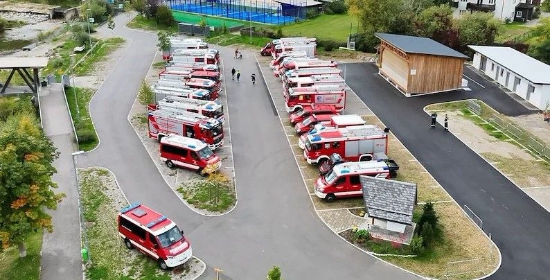 Mehrere Feuerwehrfahrzeuge stehen geparkt, Menschen üben für einen Feuerwehreinsatz.