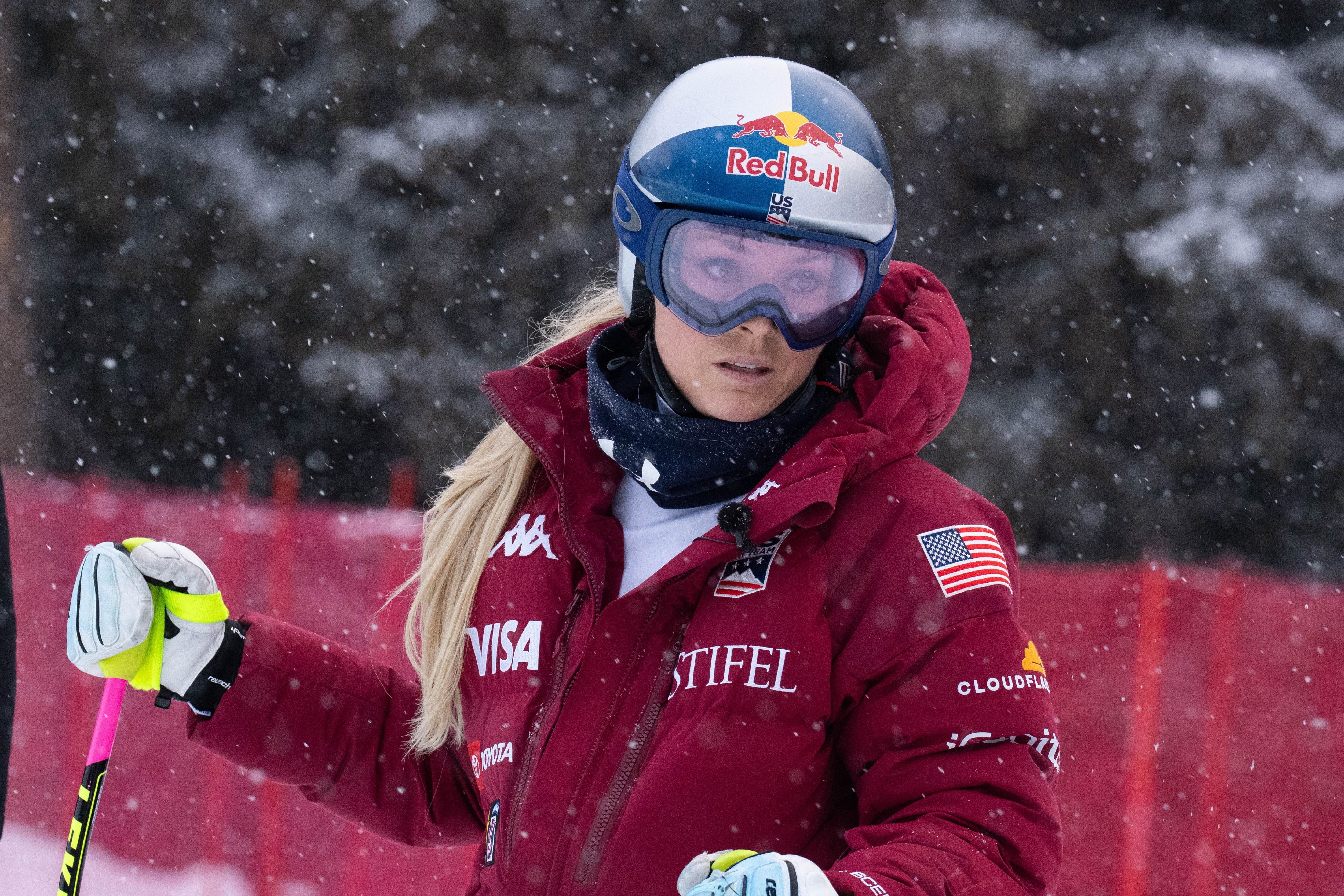 Skirennläuferin im roten Anzug und Helm steht im Schneefall auf einer Skipiste.