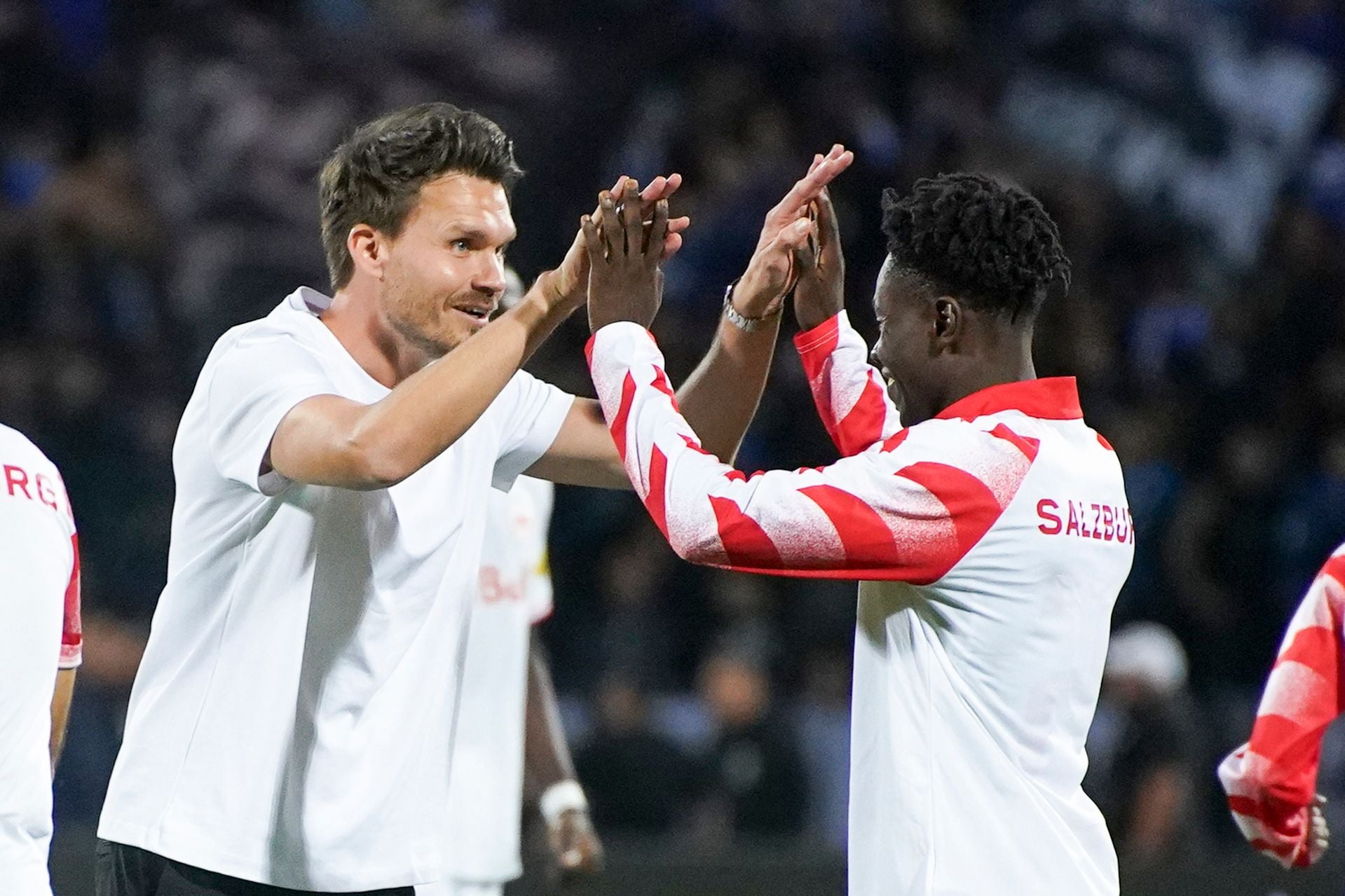 Danny Röhl und ein Spieler des FC Salzburg klatschen mit beiden Händen lächelnd auf dem Spielfeld ab.