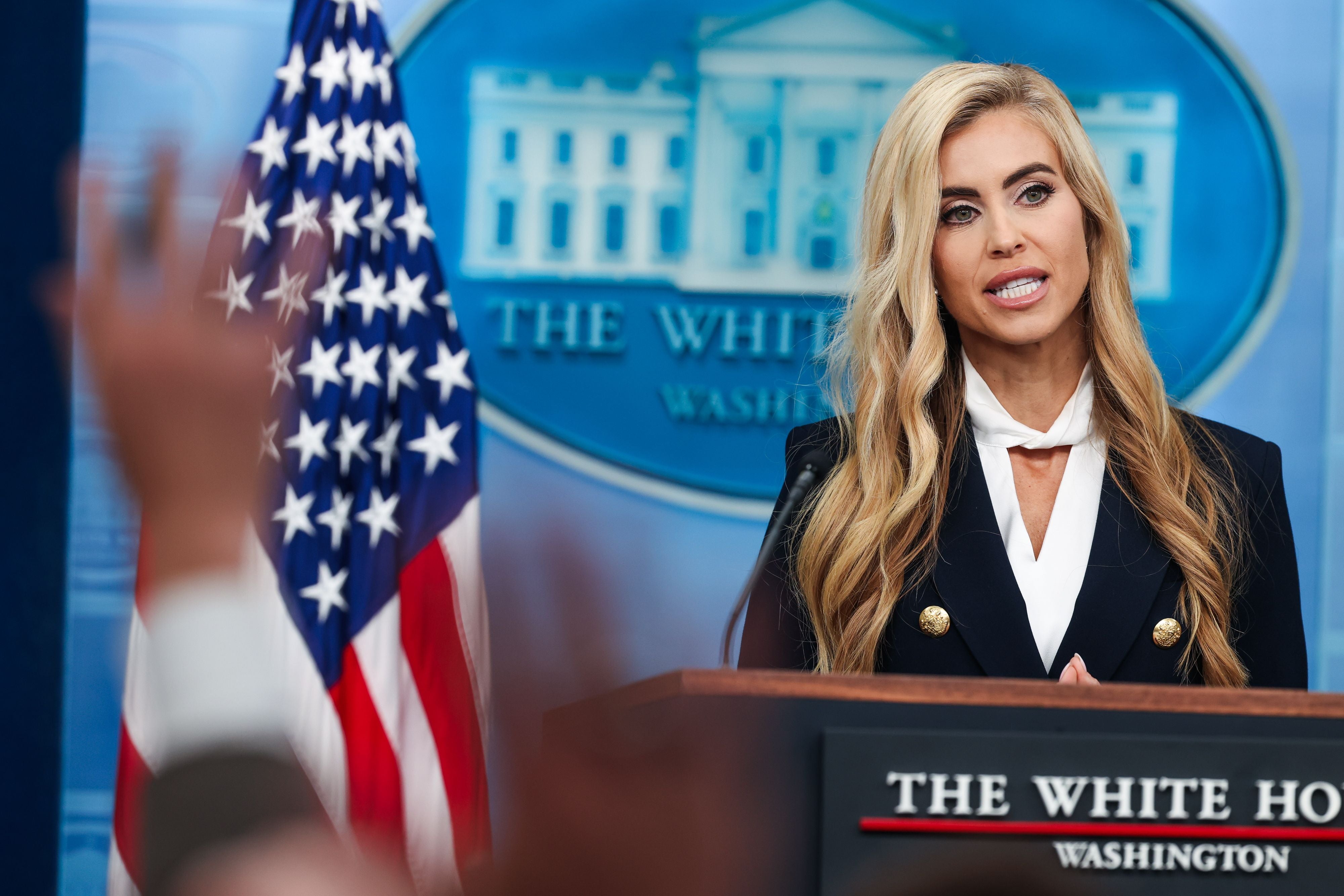 Eine Frau spricht bei einer Pressekonferenz im Weißen Haus, mit US-Flagge im Hintergrund.
