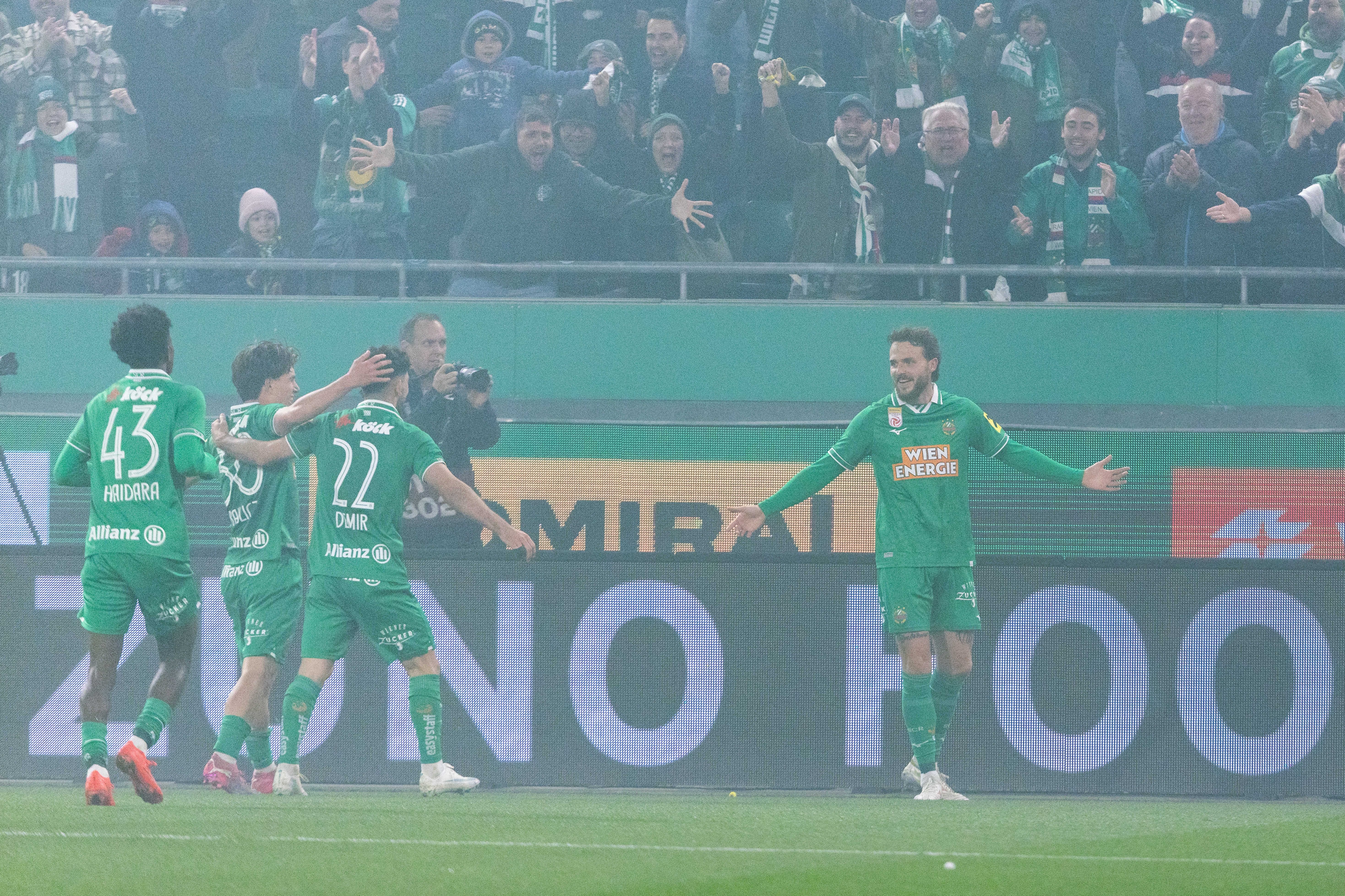Jannes Horn läuft mit ausgebreiteten Armen im Nebel über den Rasen und feiert seinen Treffer gemeinsam mit seinen jubelnden Rapid-Teamkollegen.