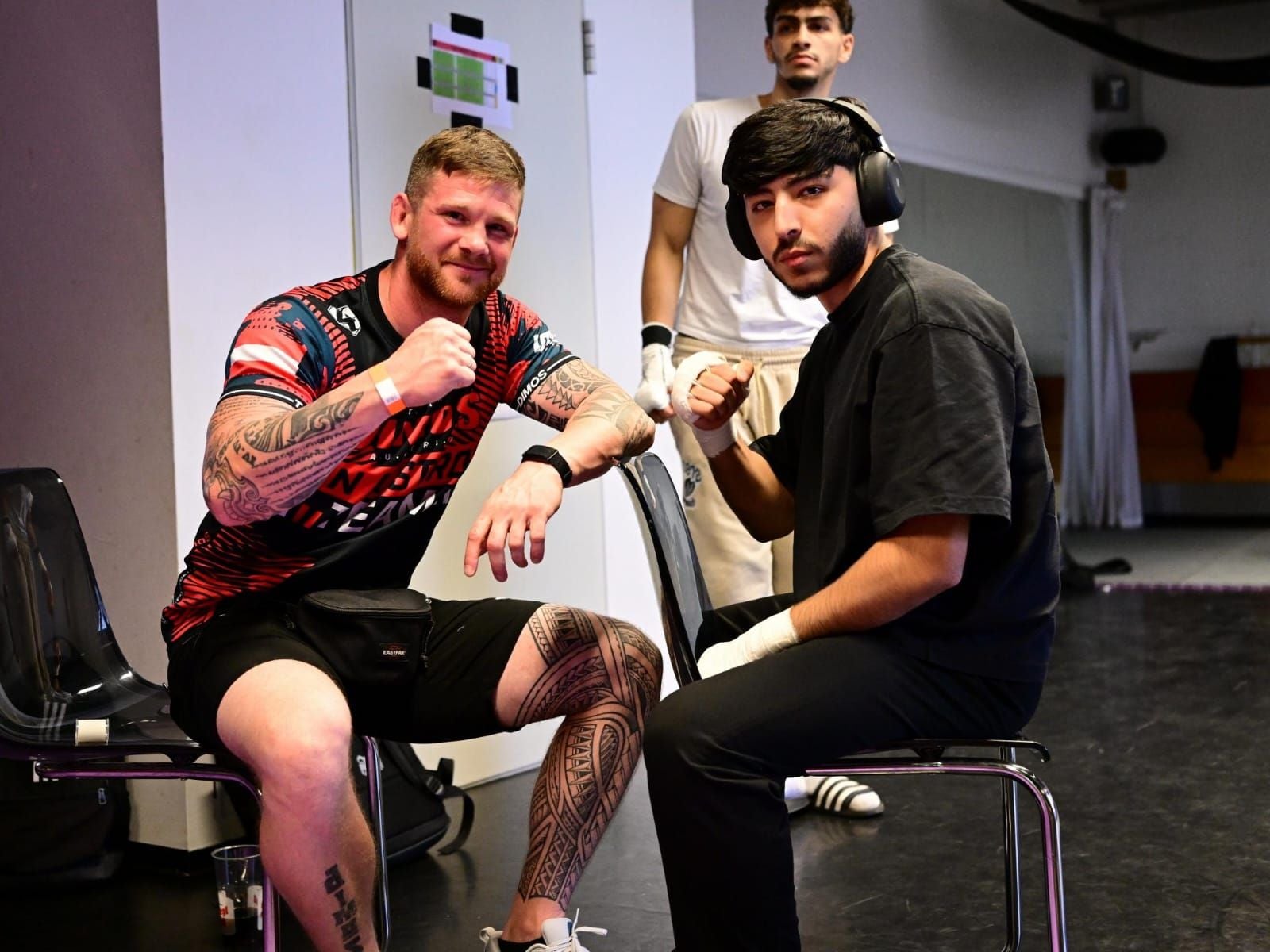 Zwei Männer posieren im Dimos Kampfsportcenter, ein dritter steht im Hintergrund.
