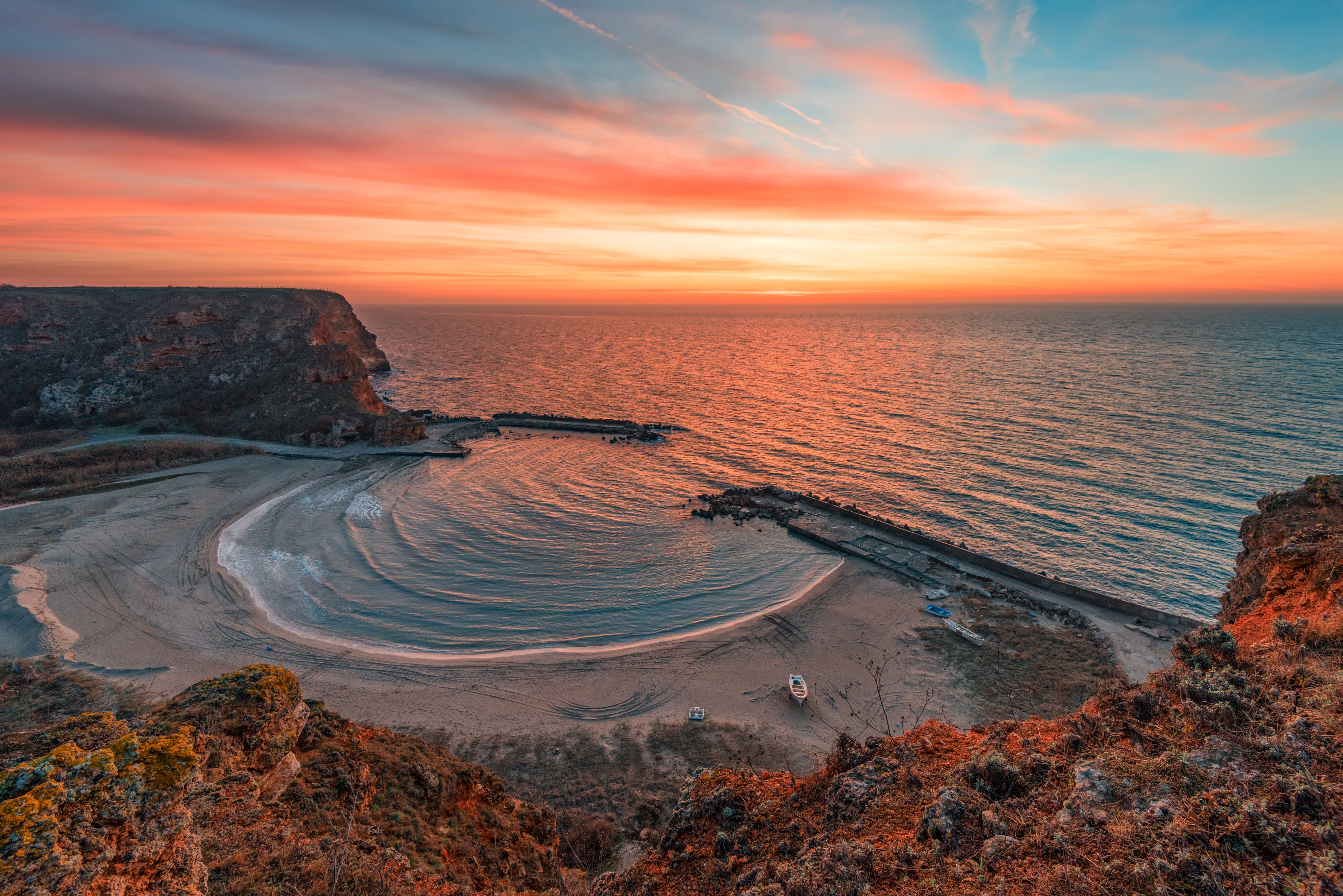Klippenbucht mit Sandstrand bei Sonnenaufgang, orangefarbenes Licht und ruhiges Meer.
