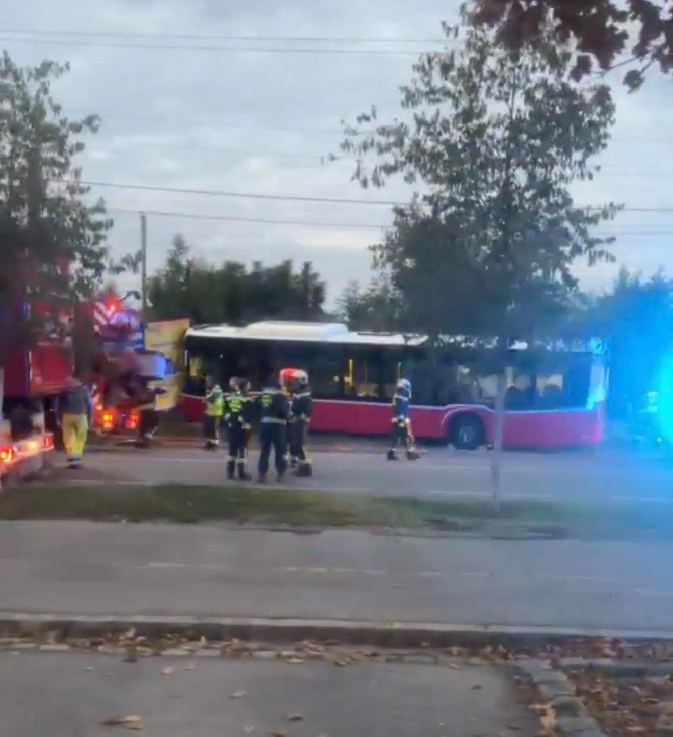 Feuerwehrleute stehen vor einem roten Linienbus und Einsatzfahrzeugen auf einer Straße.