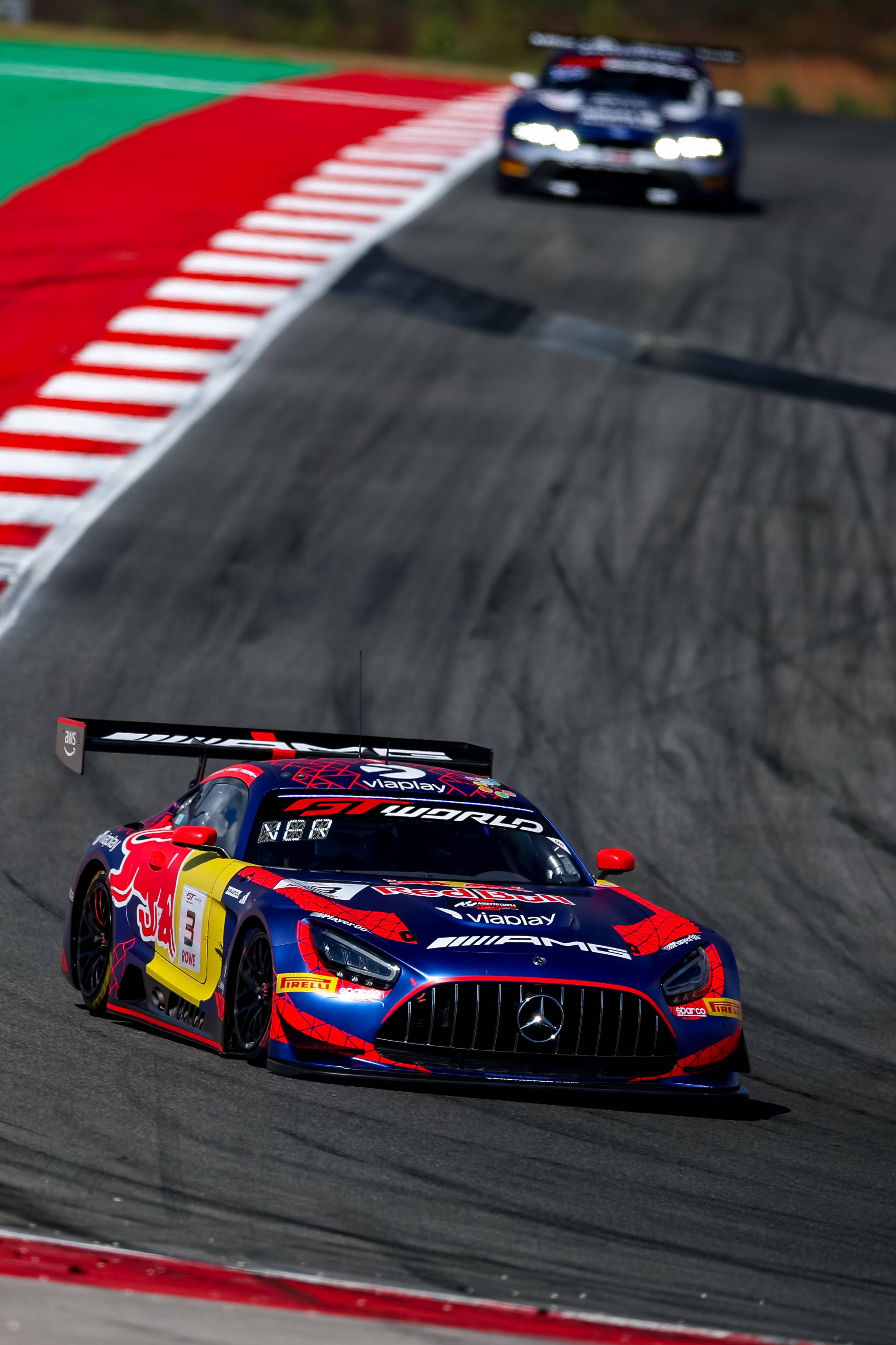 Ein farbenfroher Mercedes-AMG GT3-Rennwagen fährt auf einer Kurve einer Rennstrecke.