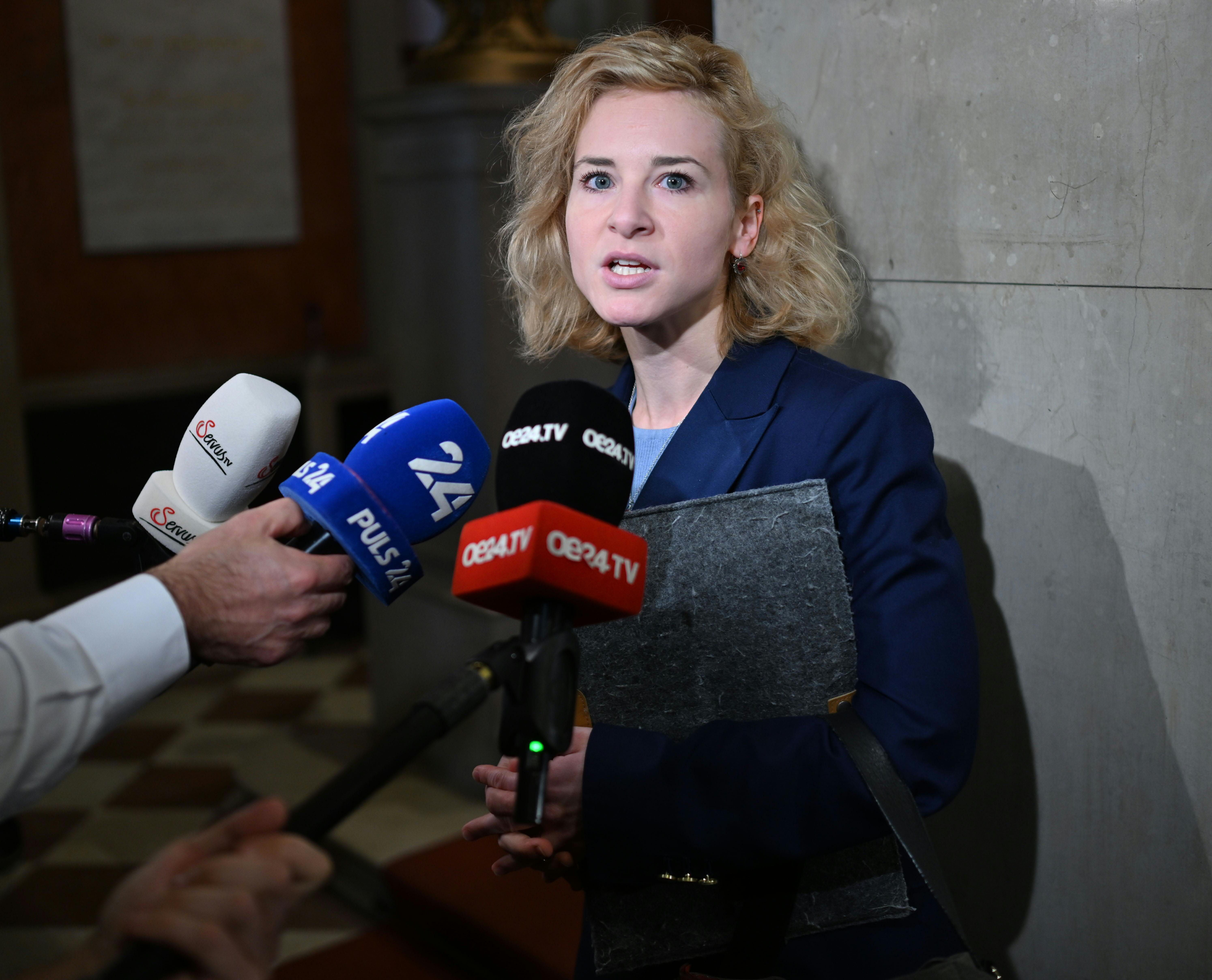 Eine Frau im blauen Blazer spricht vor mehreren Mikrofonen zu Journalisten im Parlament.