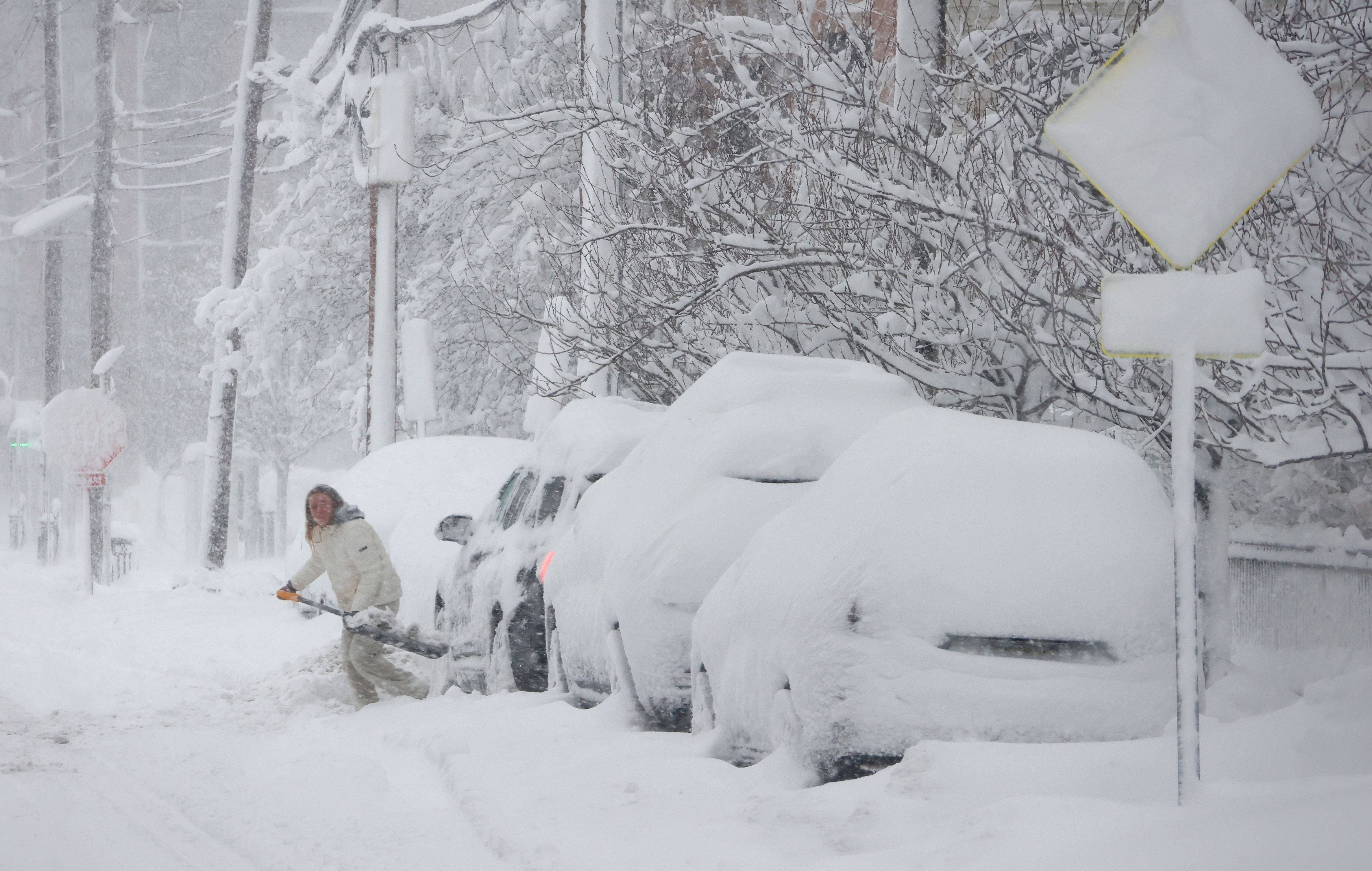 Eine Person schaufelt Schnee von einem Auto auf einer von Schnee bedeckten Straße in Hoboken.